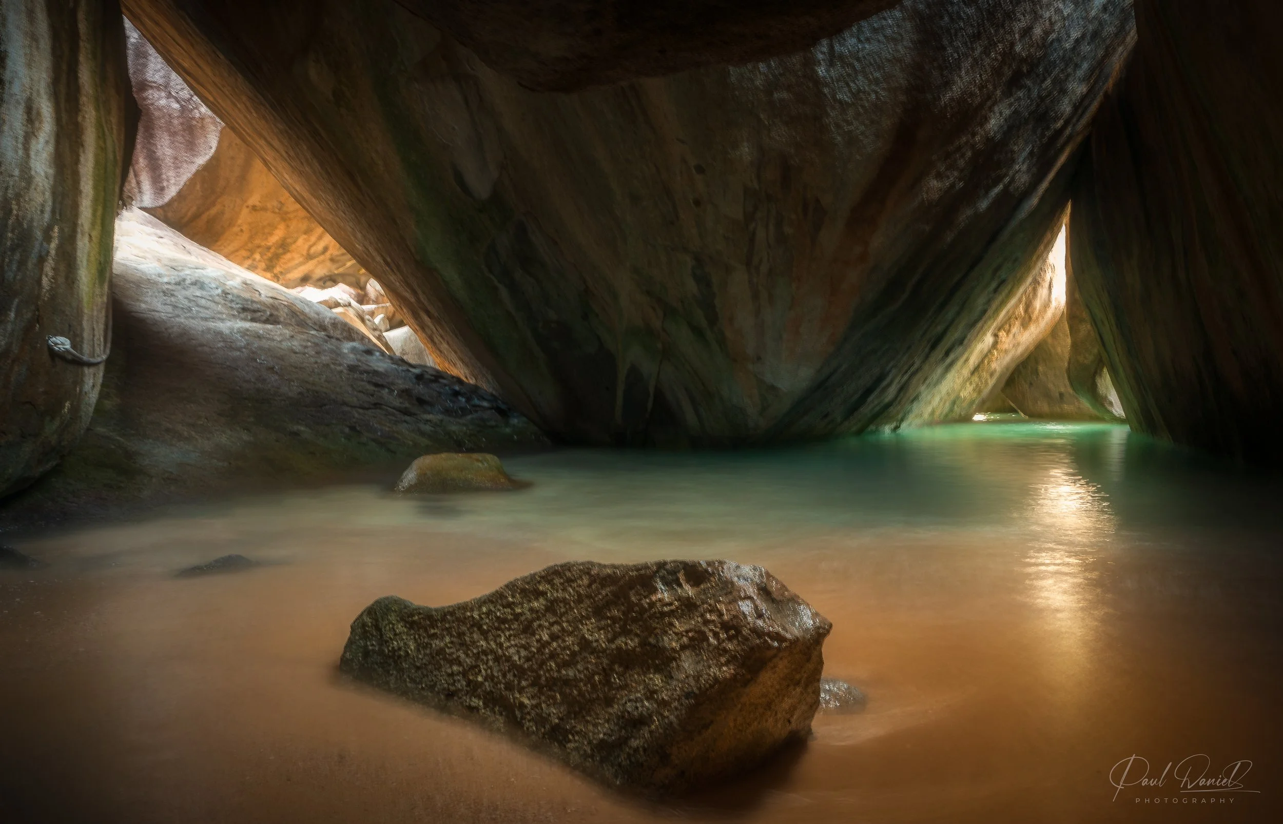 Interior view of the illuminated sea cave and tidal pools framed by massive granite boulders at The Baths National Park on Virgin Gorda, British Virgin Islands. 