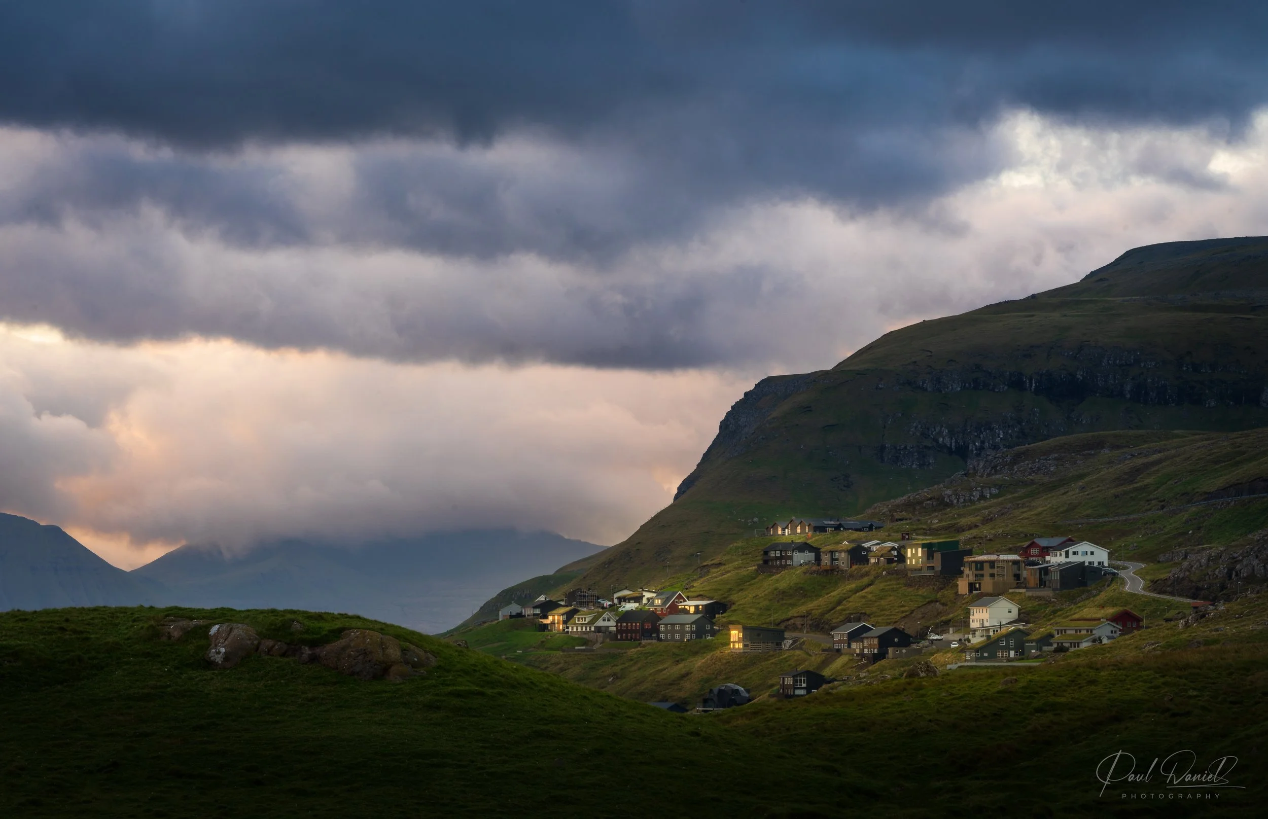 Remote hillside village lit at dusk beneath dramatic mountain skies -- Faroe Islands