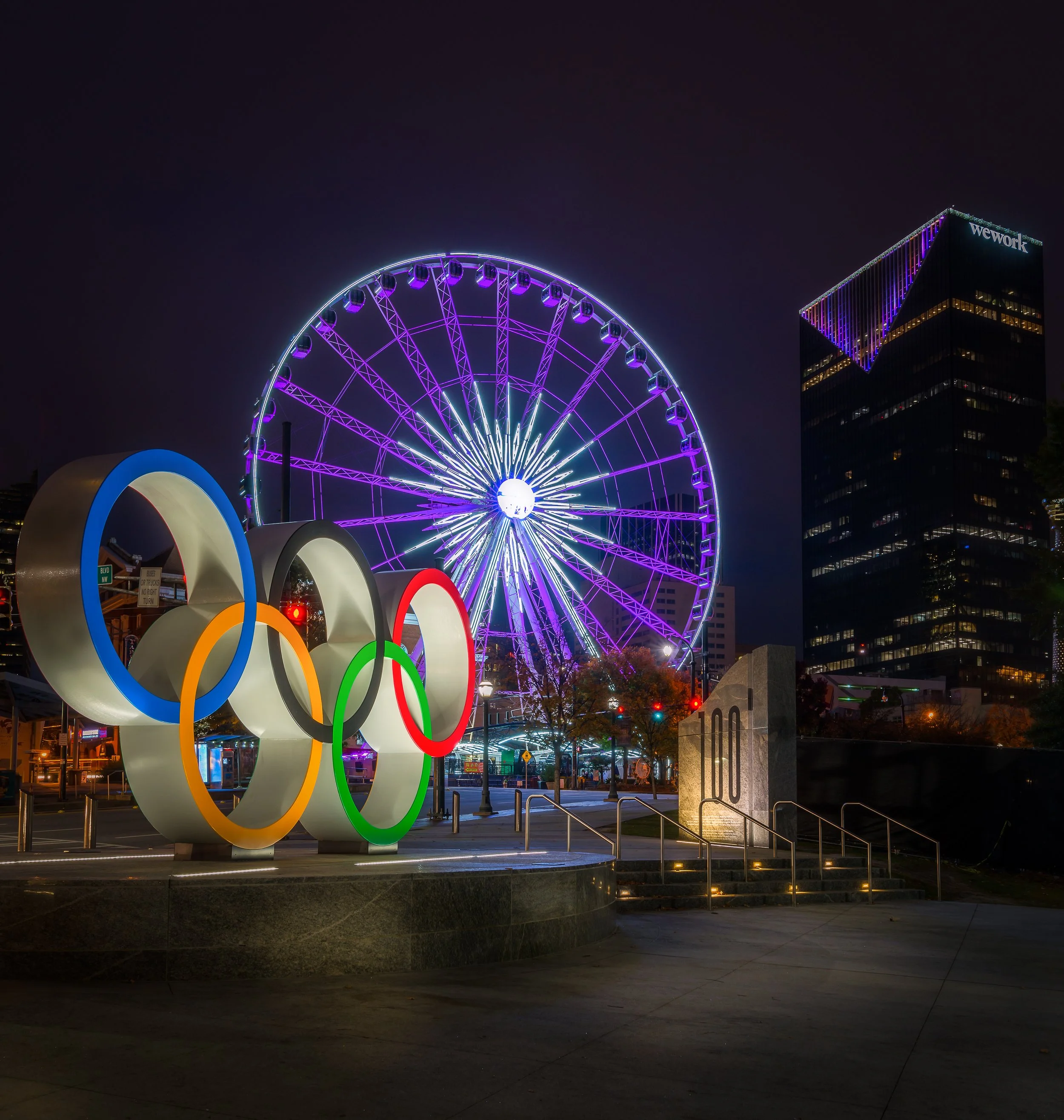 Centennial Olympic Park rings sculpture at night with the illuminated SkyView Atlanta Ferris wheel glowing purple downtown Atlanta