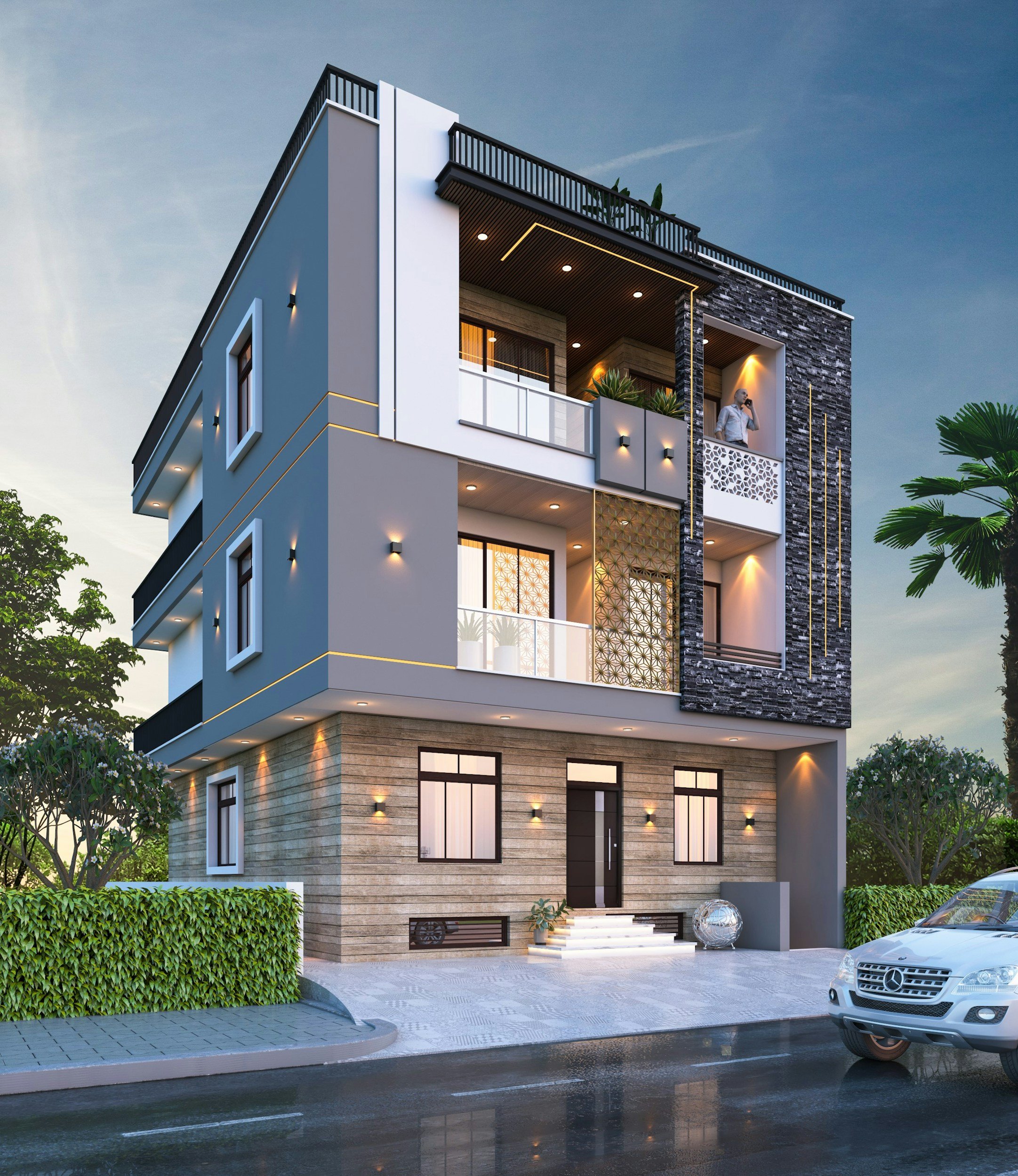 Modern multi-story house with a mix of white and stone exterior, multiple balconies with plants, large windows, outdoor lighting, and a driveway with a parked silver Mercedes-Benz car, surrounded by greenery and trees.