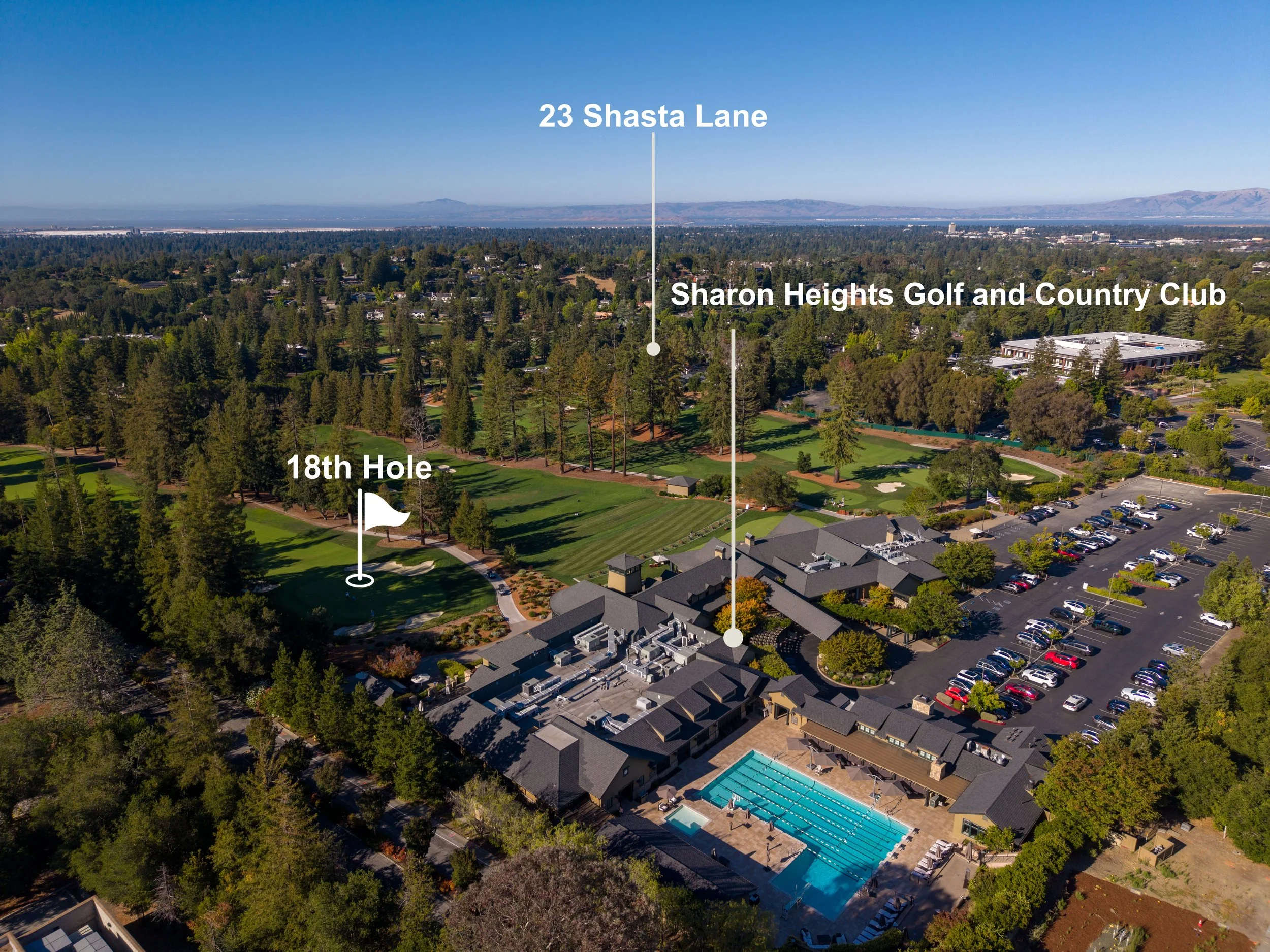 Aerial view of a golf course with lush green fairways, a swimming pool, and nearby residential buildings, with a parking lot filled with cars. Labels indicate the 18th hole, Sharon Heights Golf and Country Club, 23 Shasta Lane, and a distant mountain