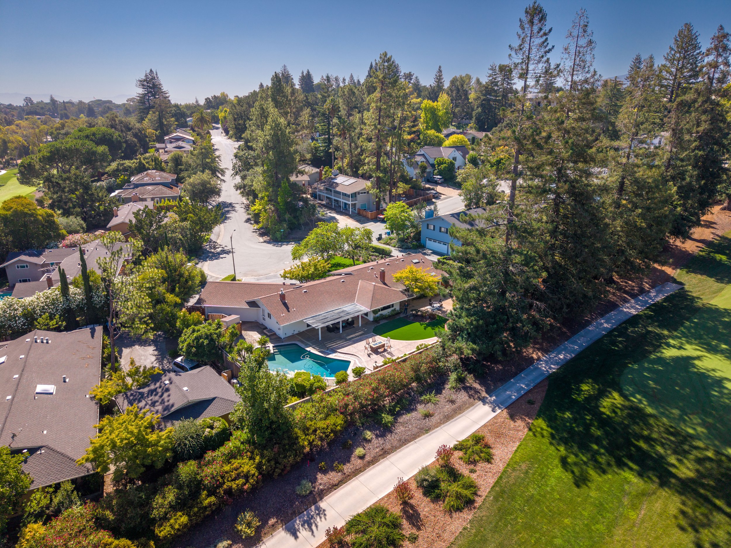 Aerial view of a suburban neighborhood with houses, trees, and a swimming pool on a sunny day.