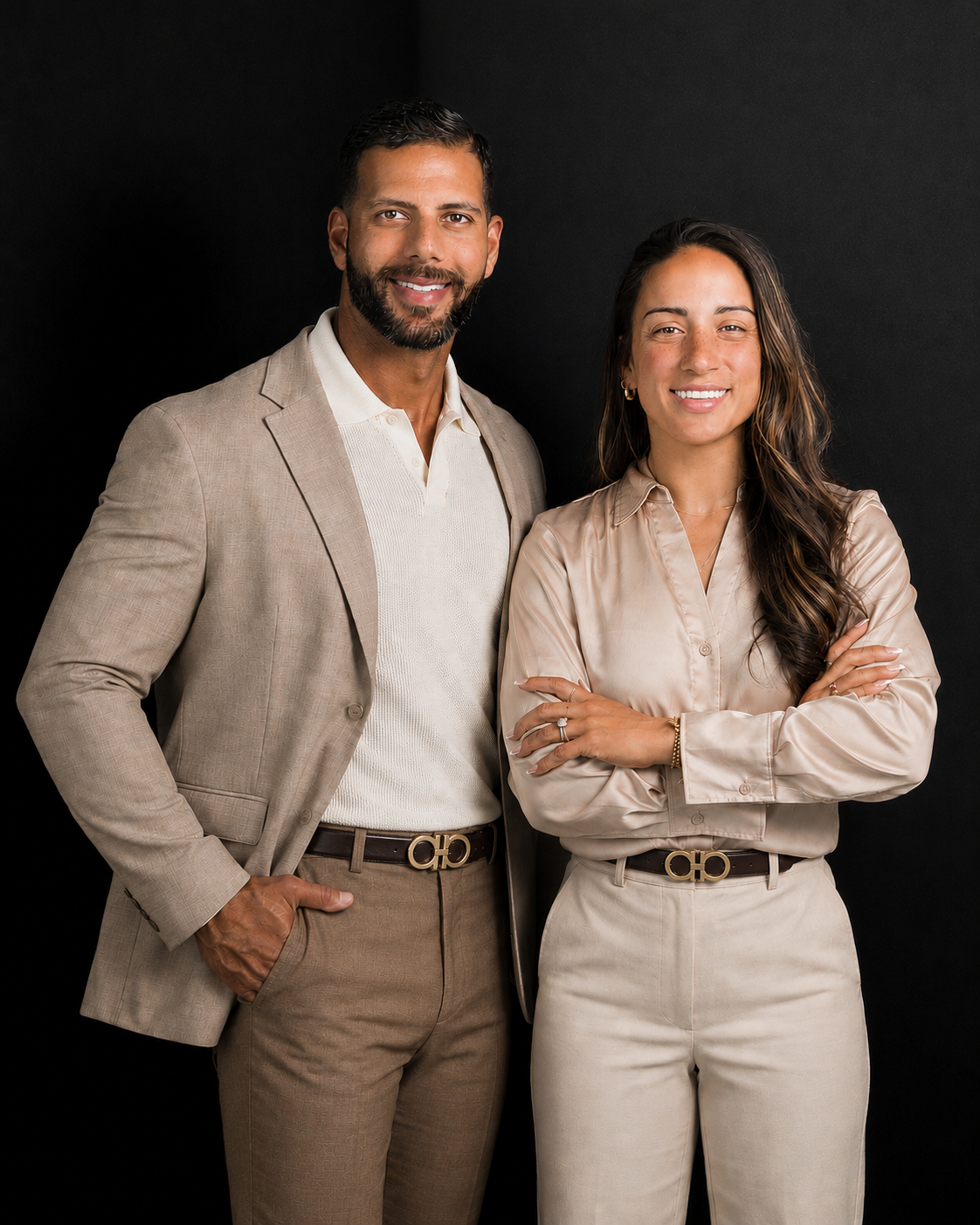 A man and a woman standing together against a black background, both dressed in beige and cream-colored business casual attire, smiling at the camera.