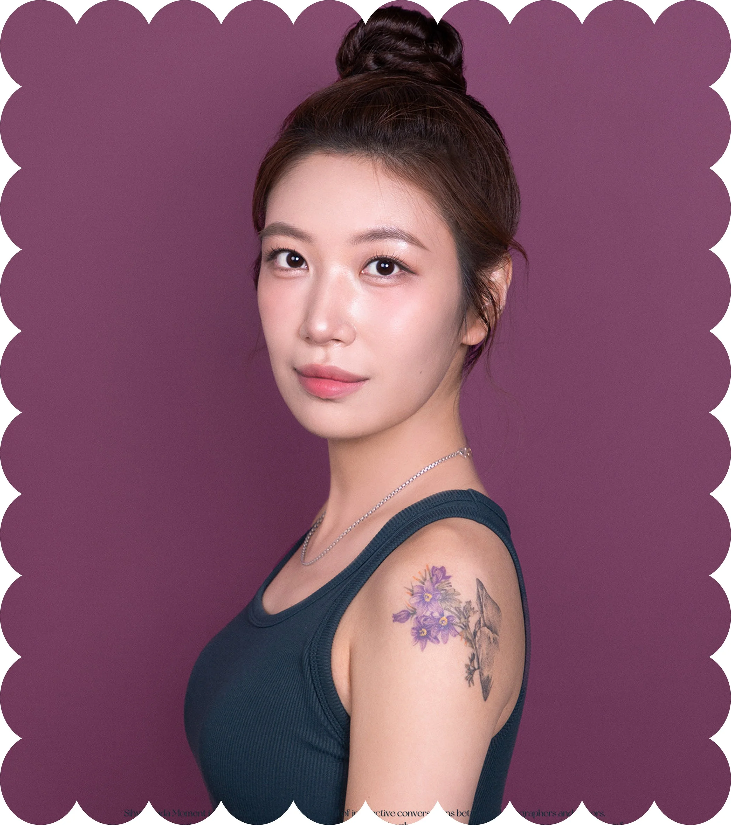 Close-up of a woman's face and upper body with floral tattoo on shoulder, wearing a black sleeveless top, against purple background.