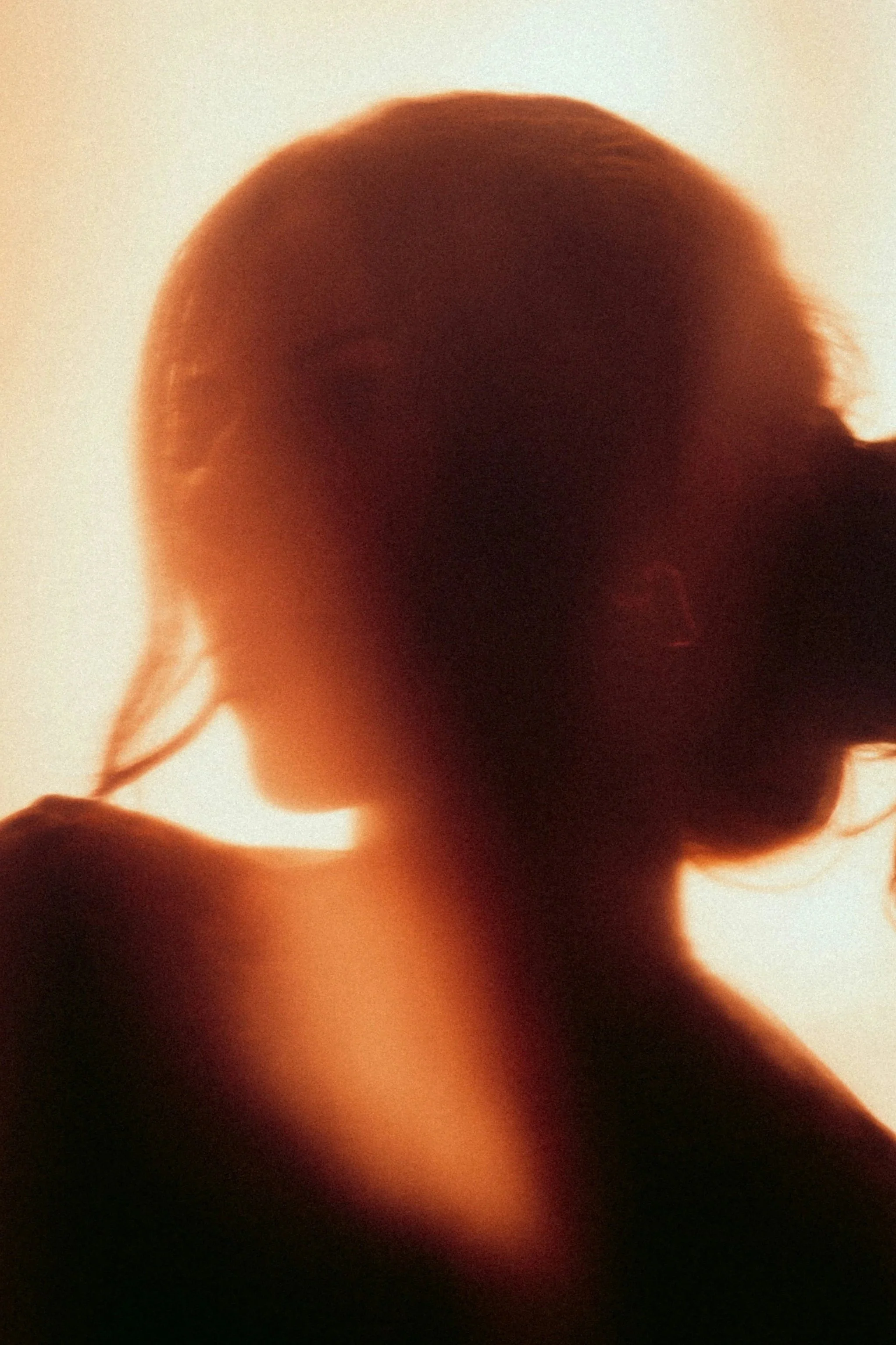 Silhouette of a woman with her hand near her face, backlit with a warm orange glow.