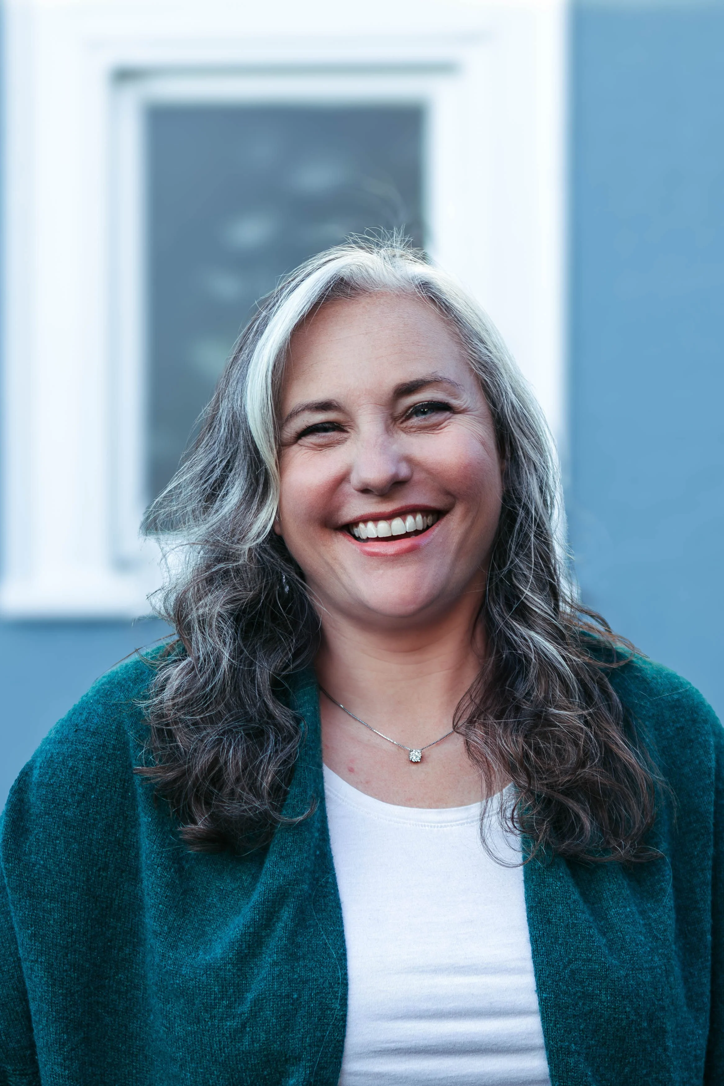picture of woman laughing wearing teal sweater with blue background.