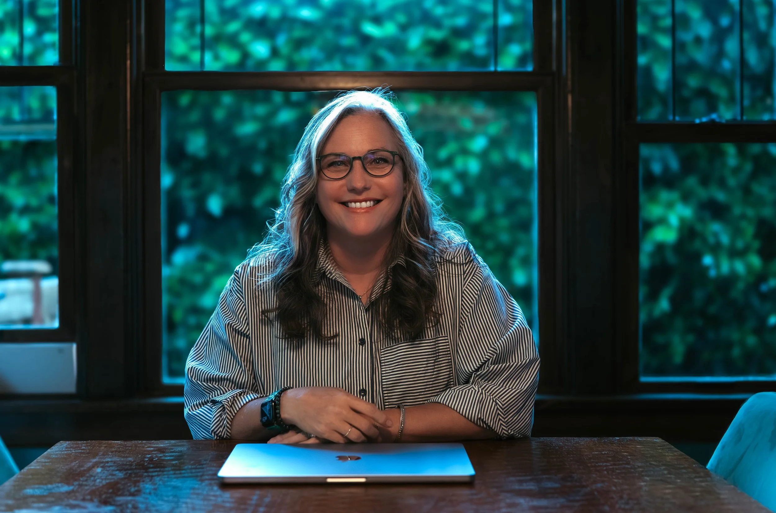 photograph of woman wearing glasses with closed computer and a alder background