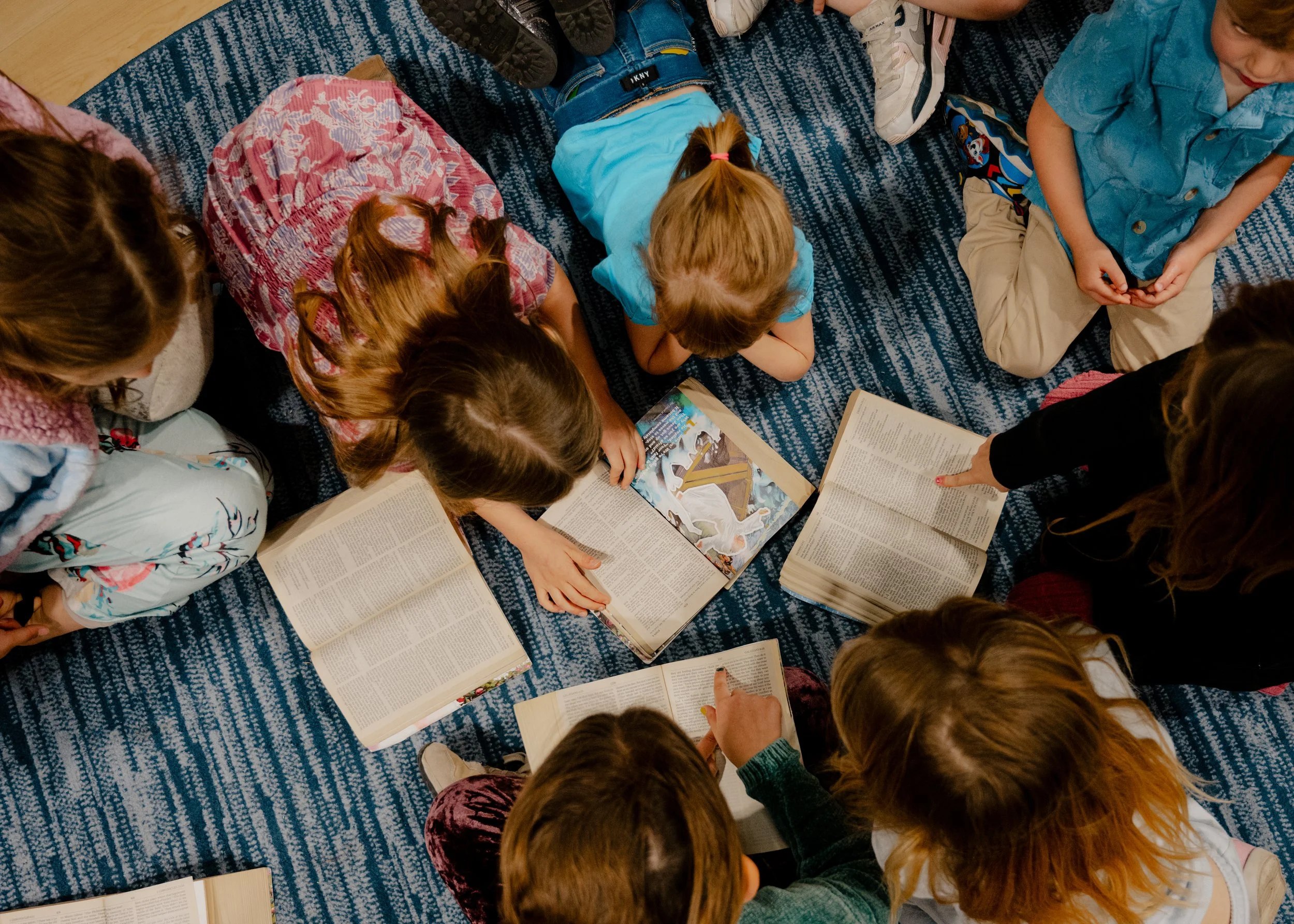 Children sitting on a blue patterned carpet, reading books.
