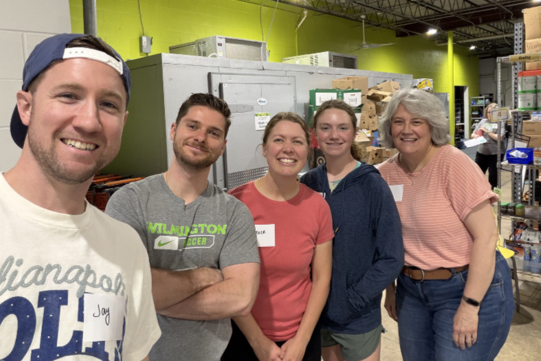 Group of five people standing together inside a warehouse, smiling at the camera.