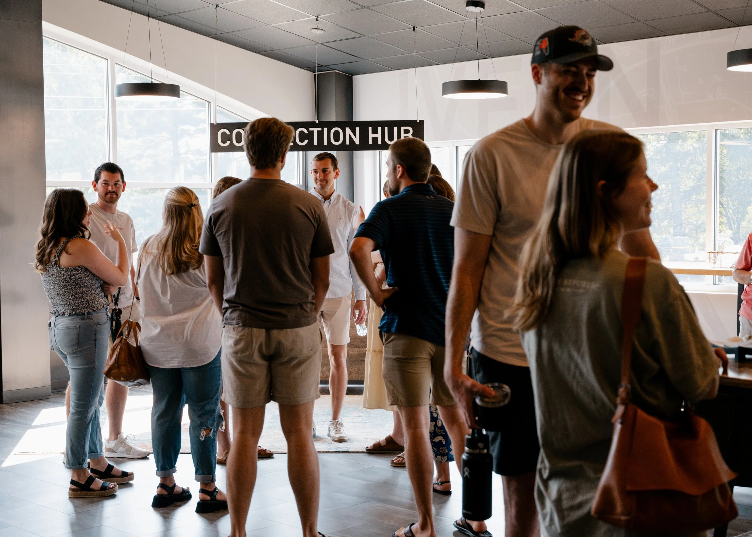 People standing and talking inside a modern building near a 'Collection Hub' sign, with large windows allowing natural light.