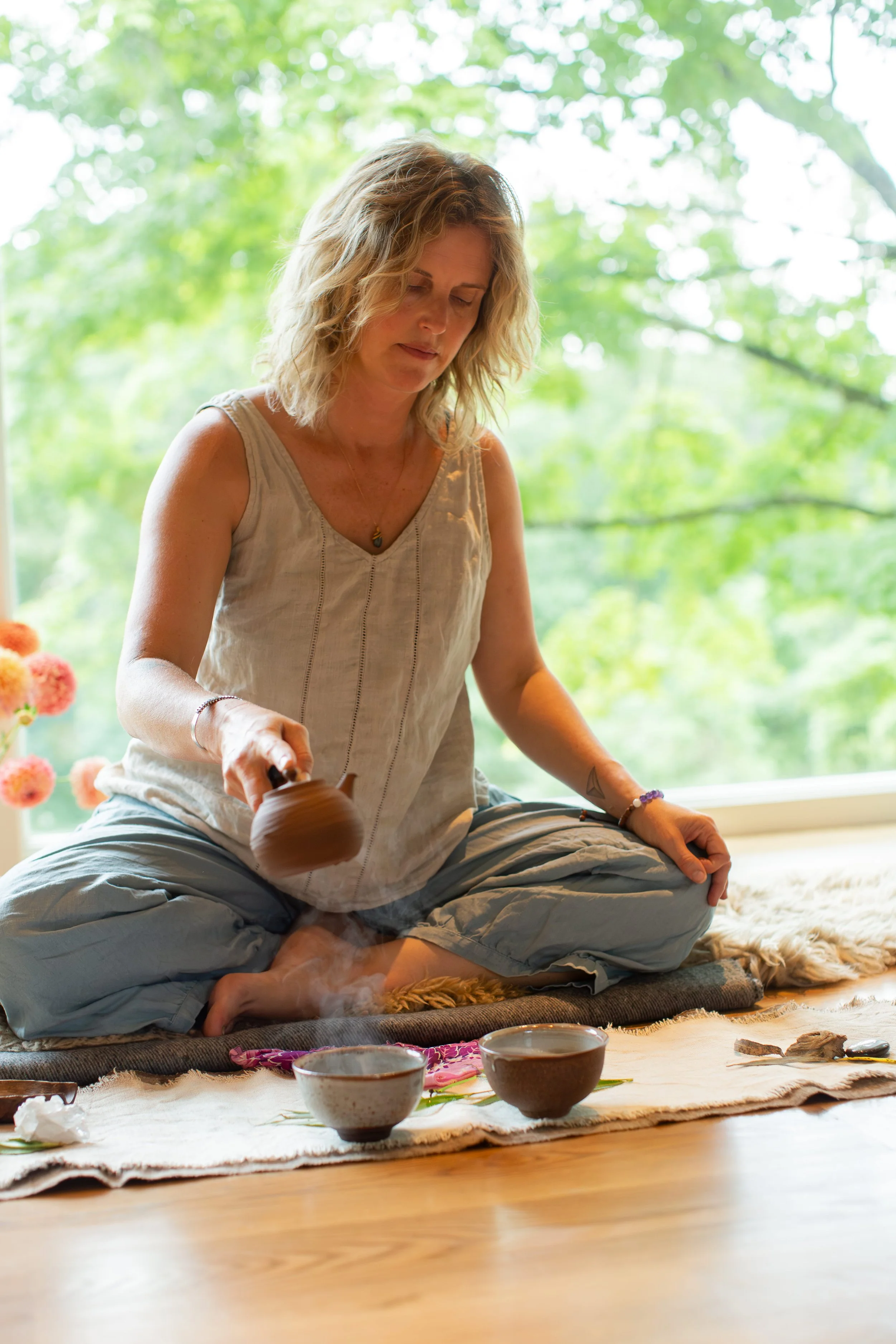 A woman performing a tea ceremony for Yoga Nidra on a mat indoors