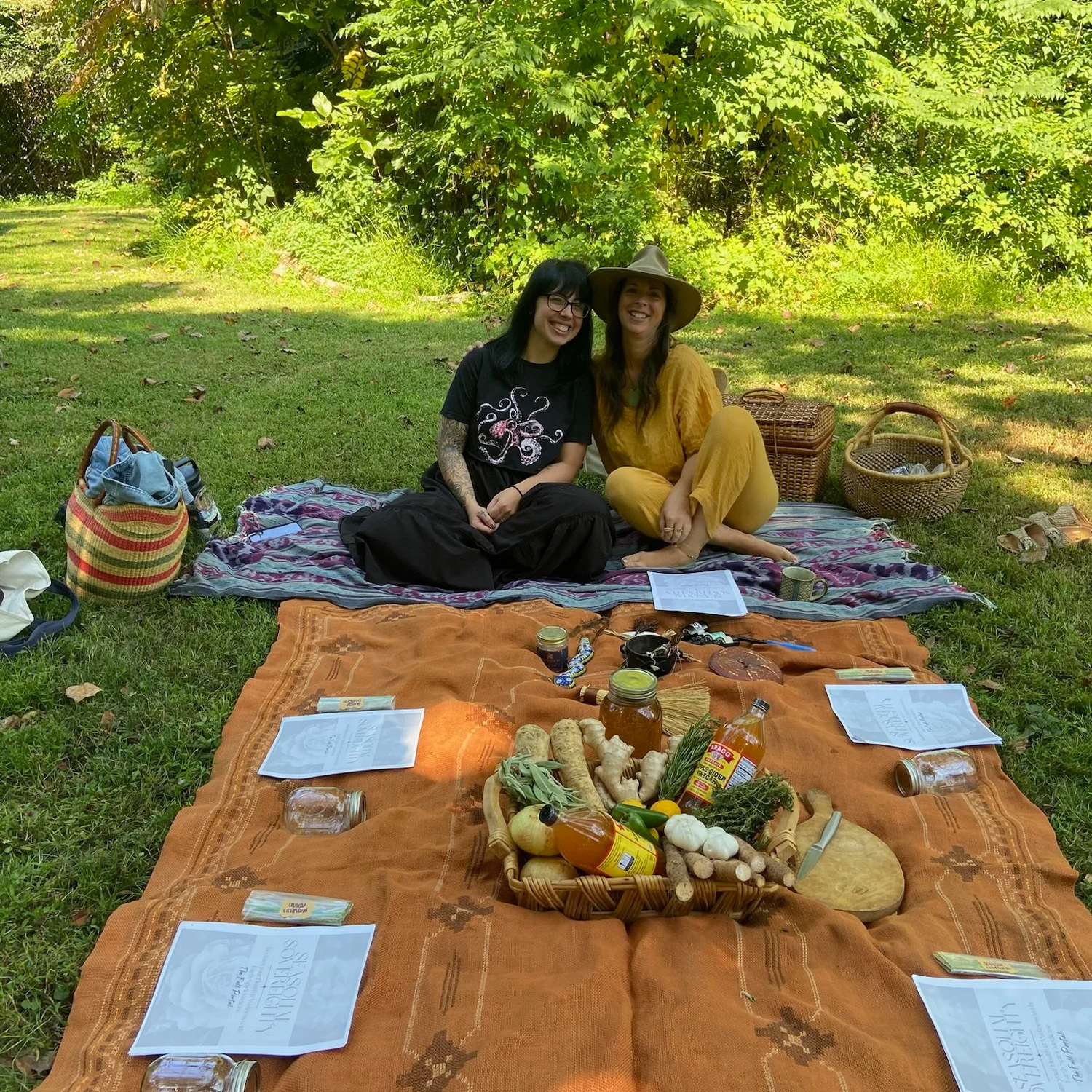 Two women surrounded by a bounty of seasonal food and herbs to be made into medicine
