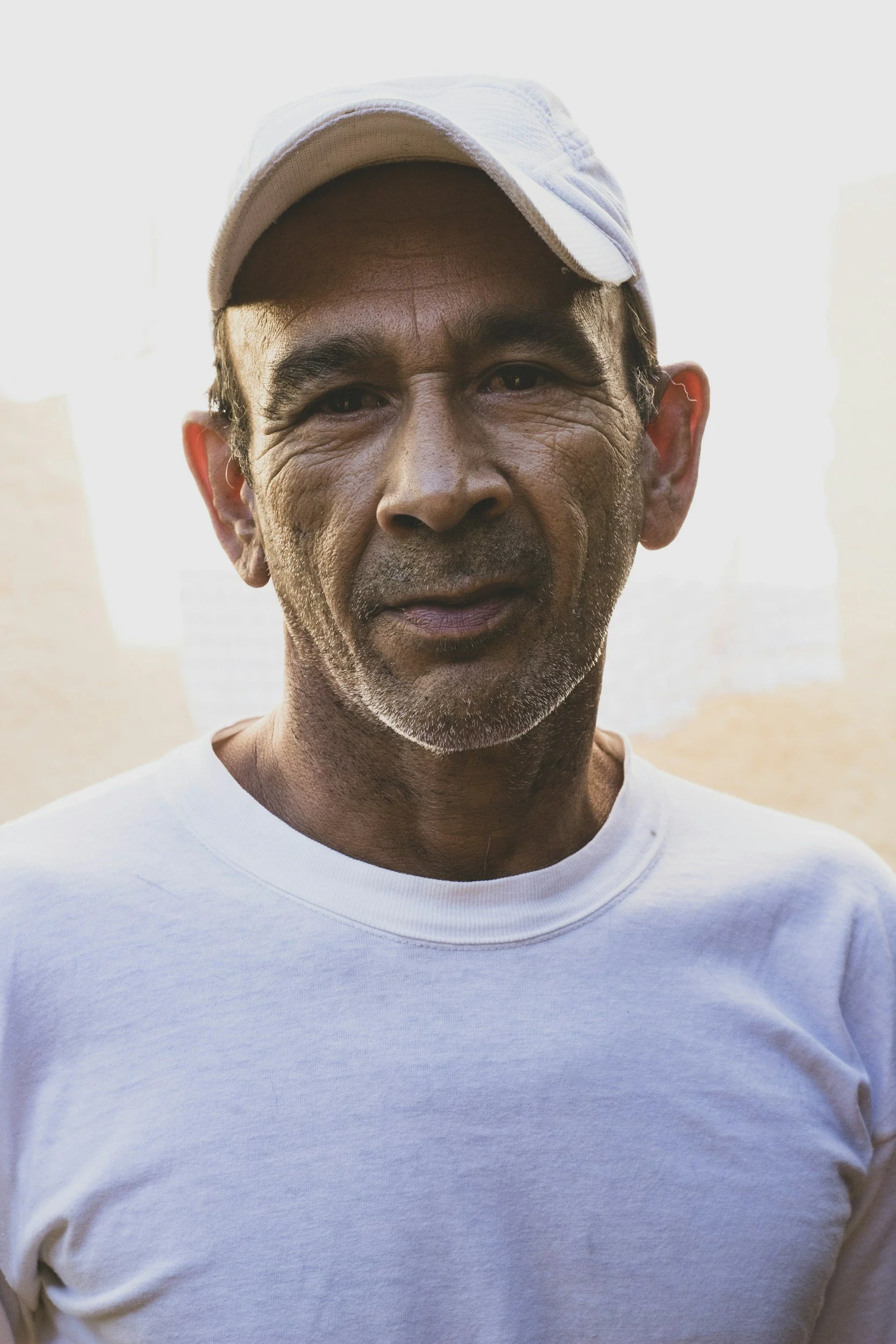 A close-up of a smiling middle-aged man wearing a white baseball cap and a white t-shirt.