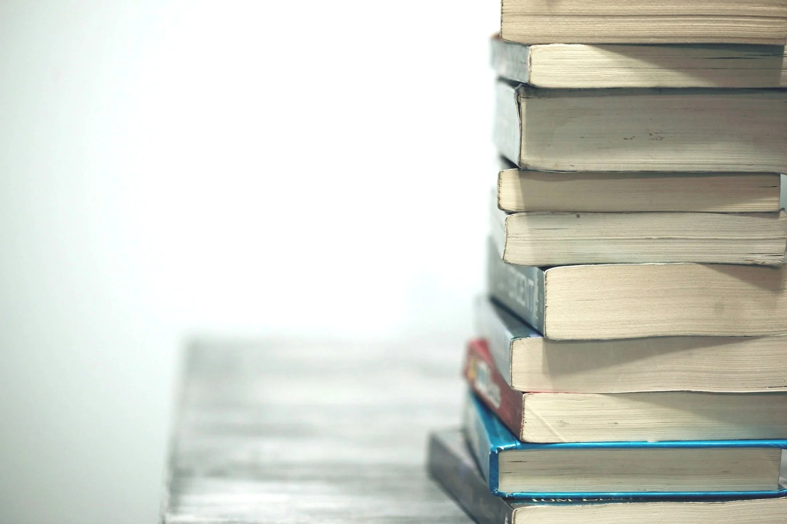 A side view of a stack of books, some with visible wear and tear, on a surface against a plain background.