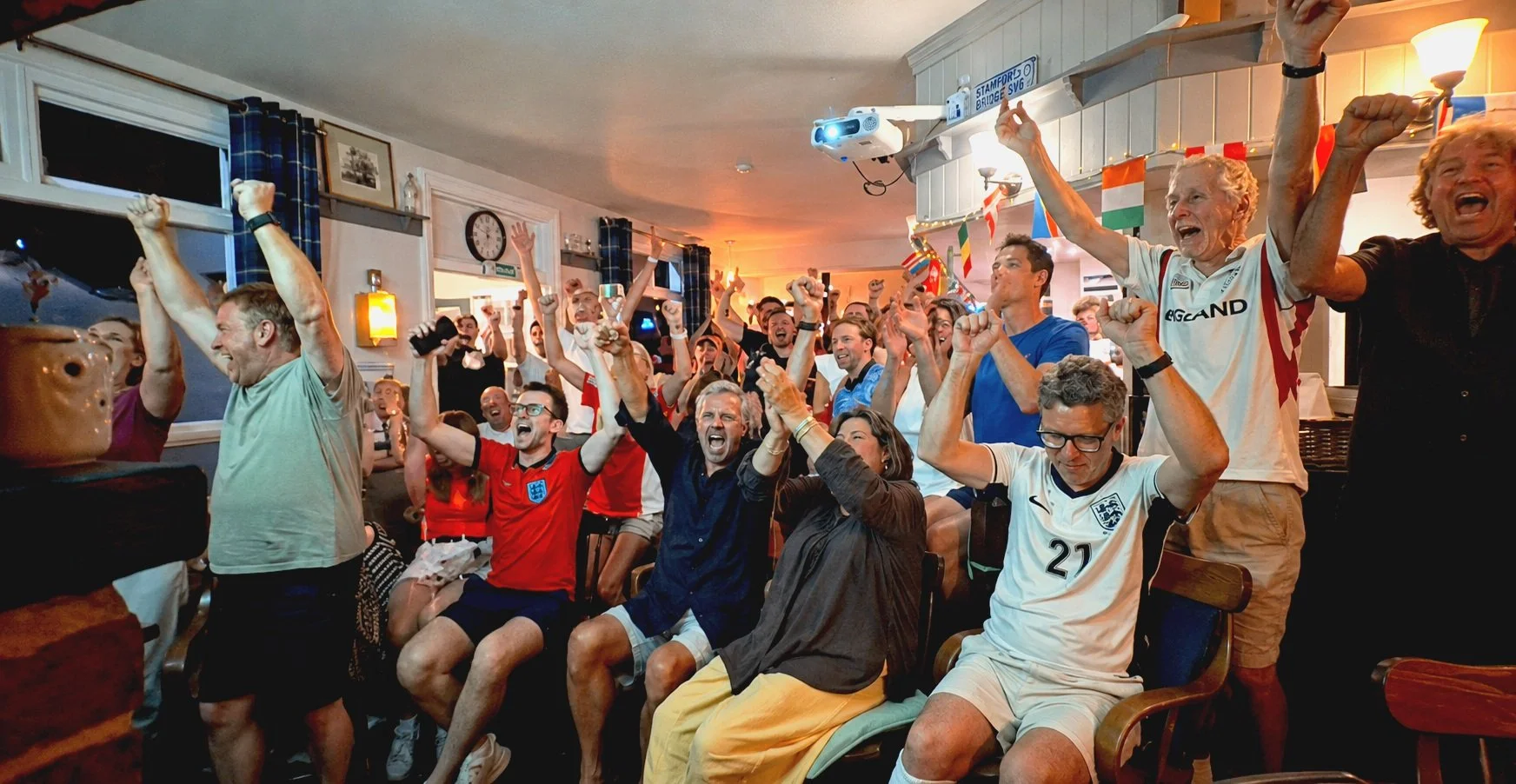 Group of people cheering and celebrating sports match victory at a pub.