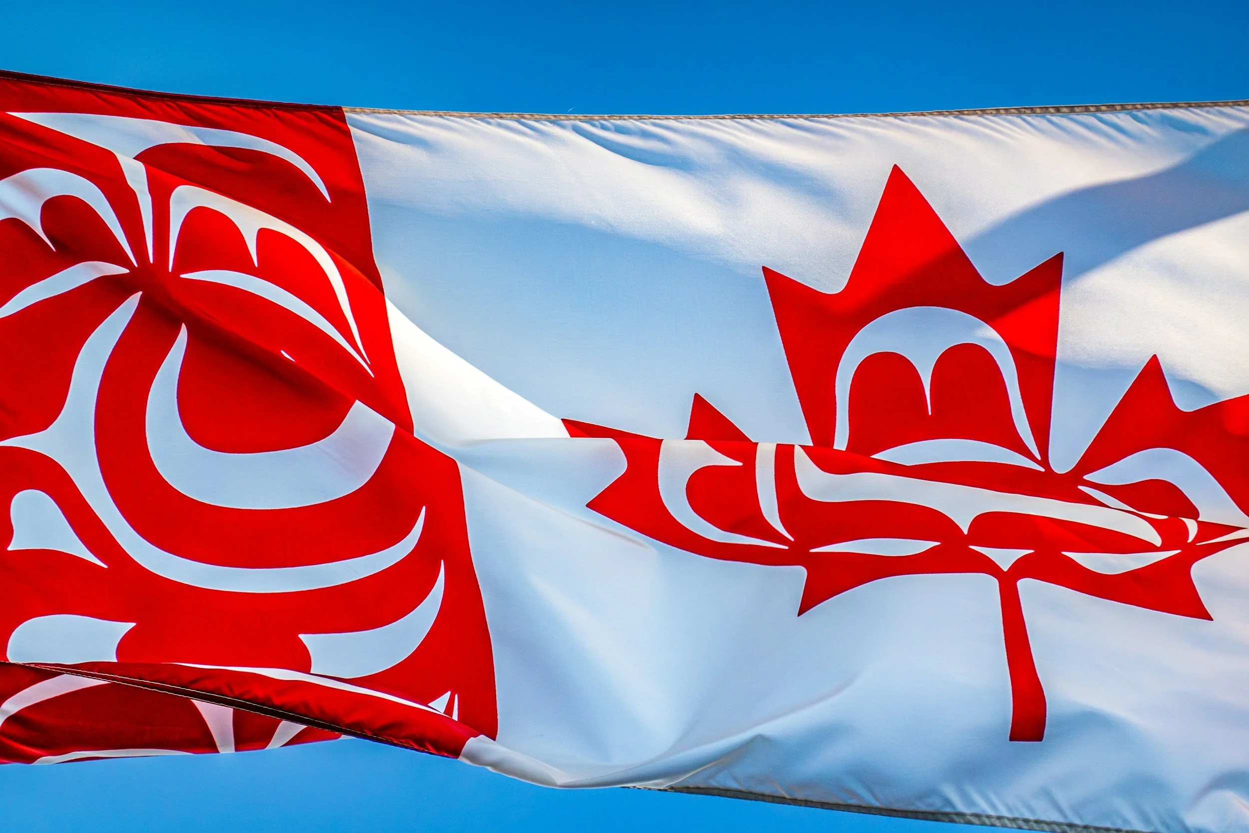 Close-up of the Canadian flag waving against a clear blue sky.