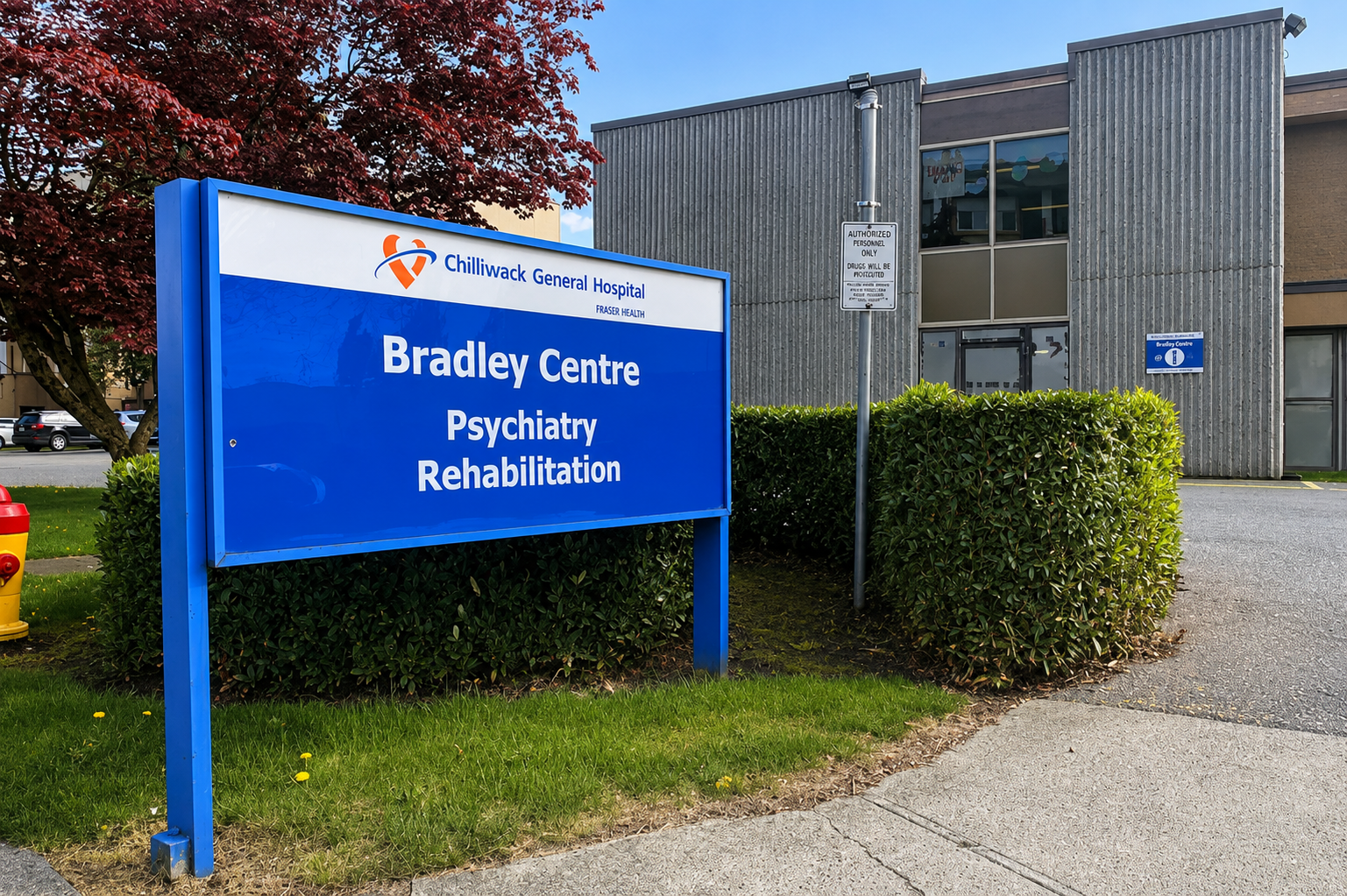 Blue sign for Bradley Centre Psychiatry Rehabilitation at Chilliwack General Hospital with a building and parking lot in the background.
