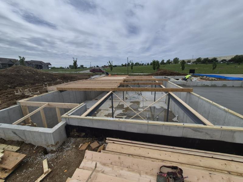 Construction site with concrete foundation and wooden framing for a building, with cloudy sky overhead.