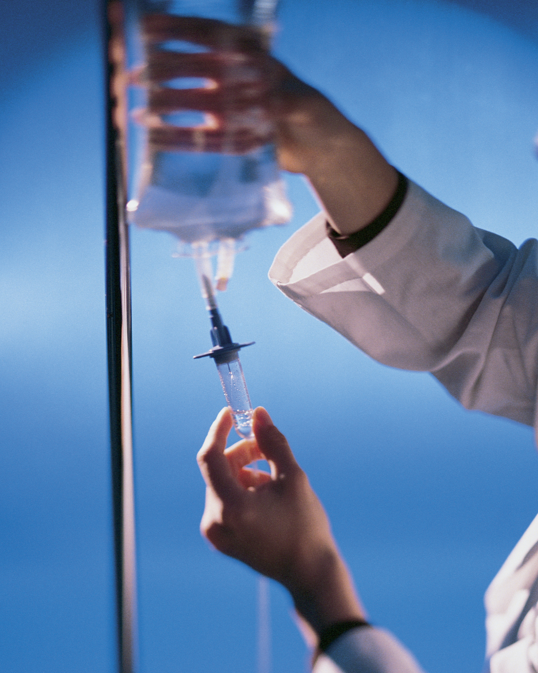 Healthcare professional drawing liquid from a vial using a syringe.