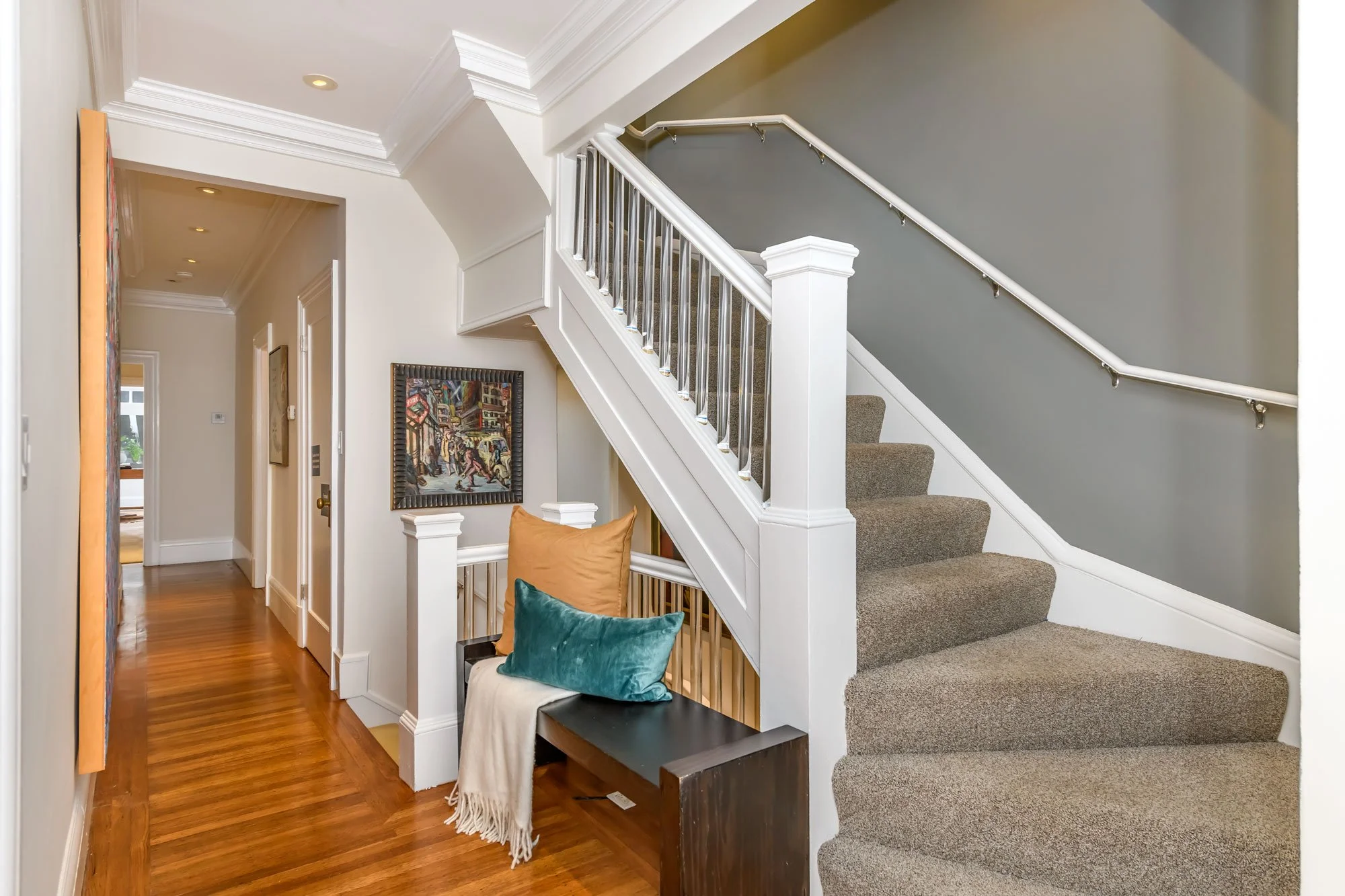 Interior view of a staircase in a home with beige carpet, white railings, and decorative accessories like pillows and framed artwork on the wall.
