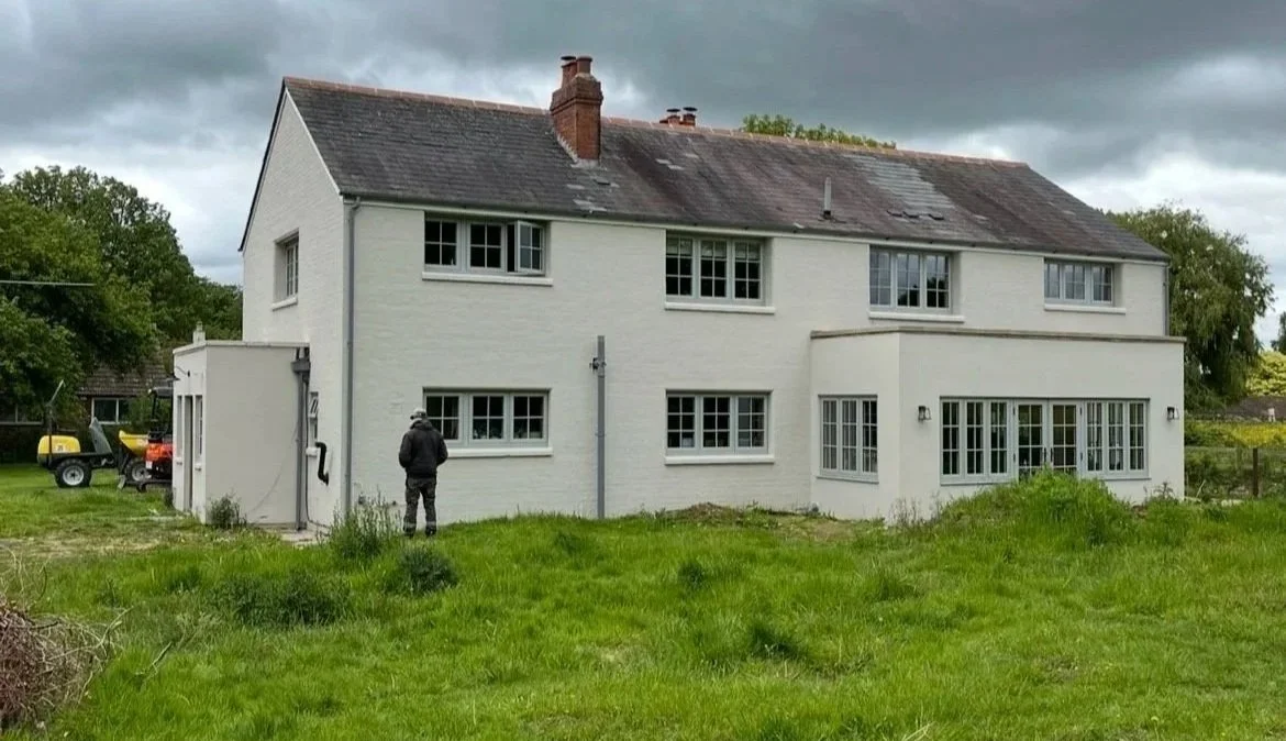 A large white house with multiple windows and a sloped roof, situated in a grassy yard on a cloudy day.