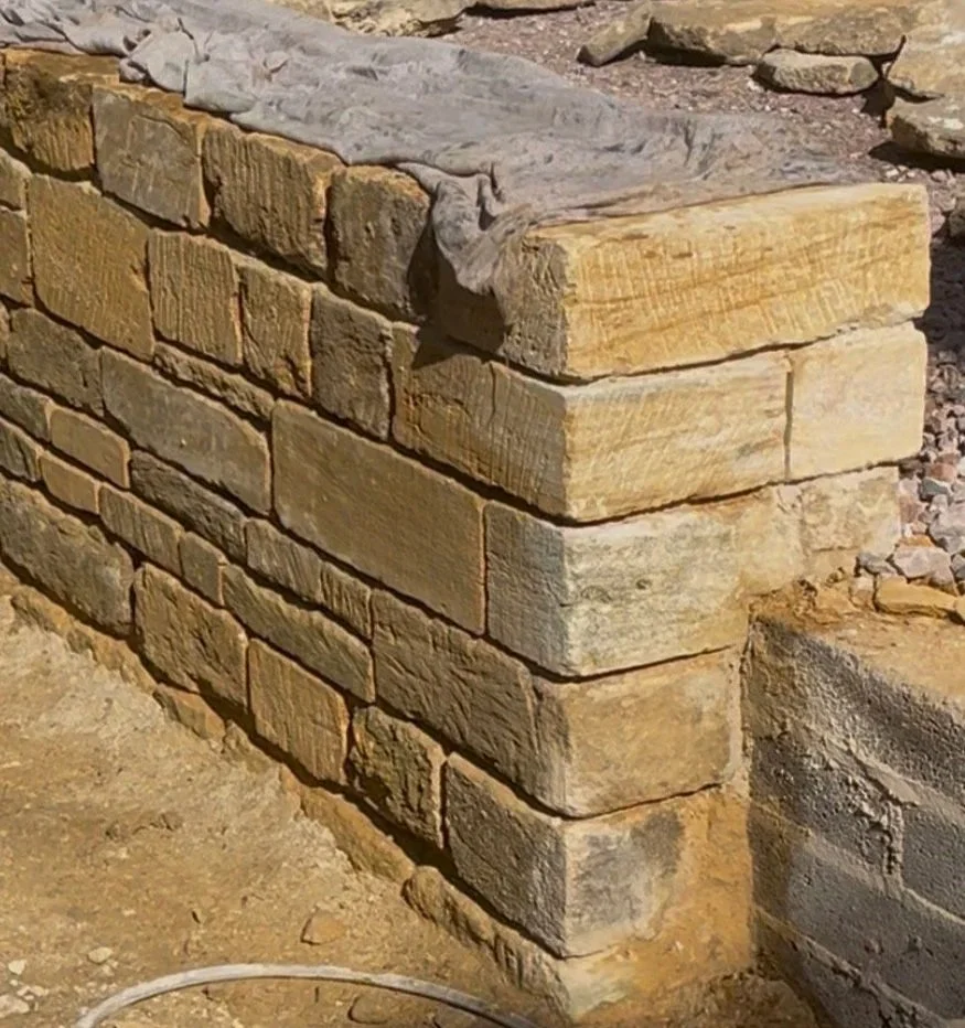 Close-up of a stone brick wall under construction with carefully stacked and aligned sandstone blocks.