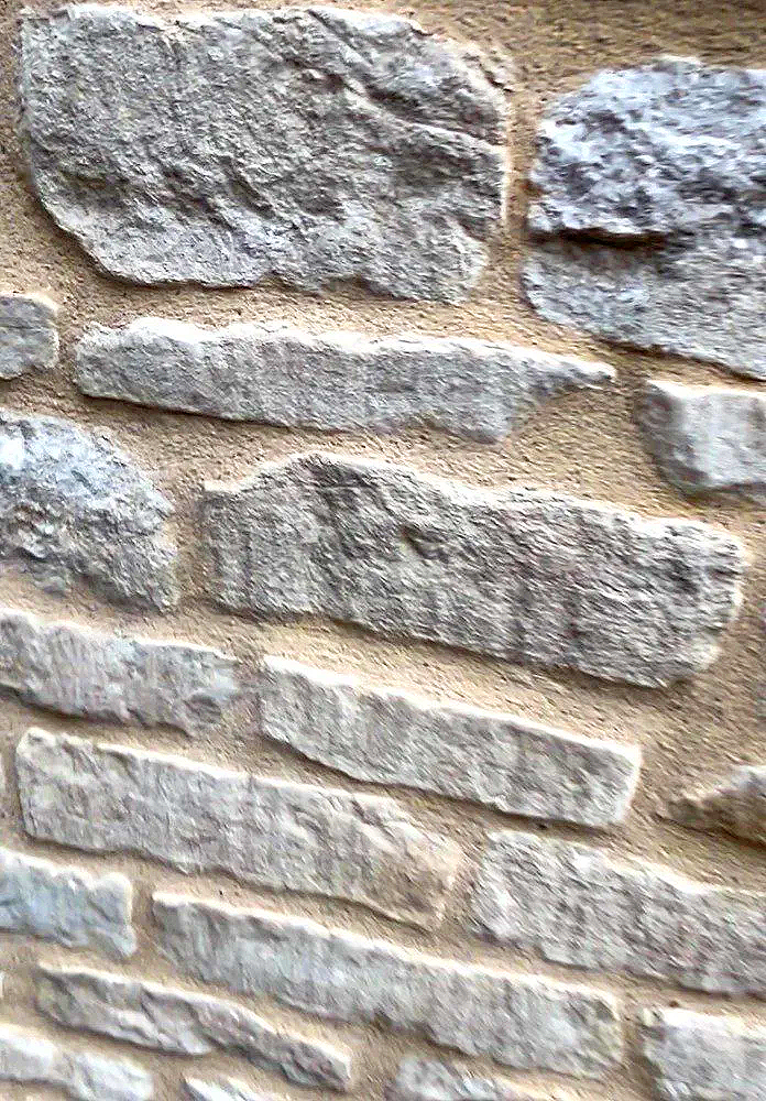 Close-up of a stone wall made with uneven rectangular gray stones and mortar.