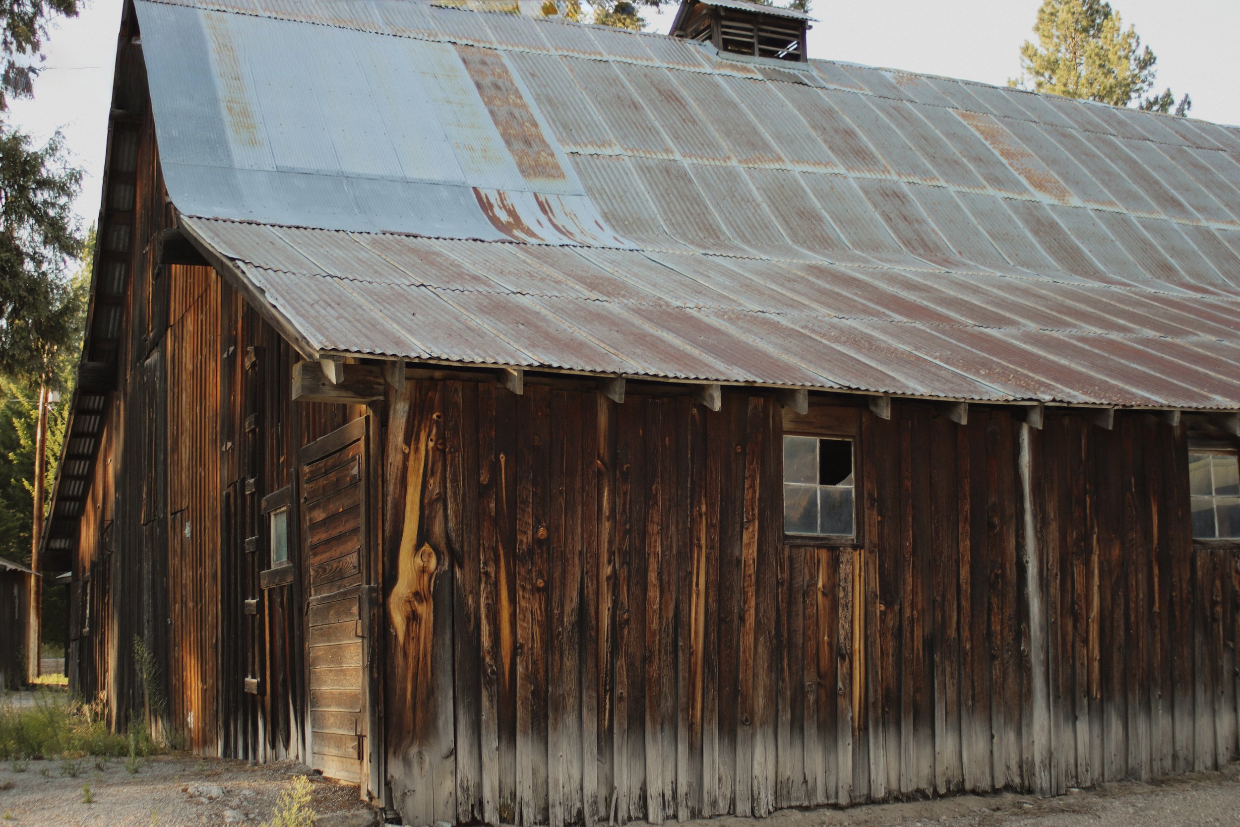 An old wooden barn with a rusted metal roof surrounded by trees.