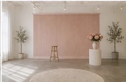 Minimalist interior with pink wall, wooden stool, large potted flowers, and two potted trees.