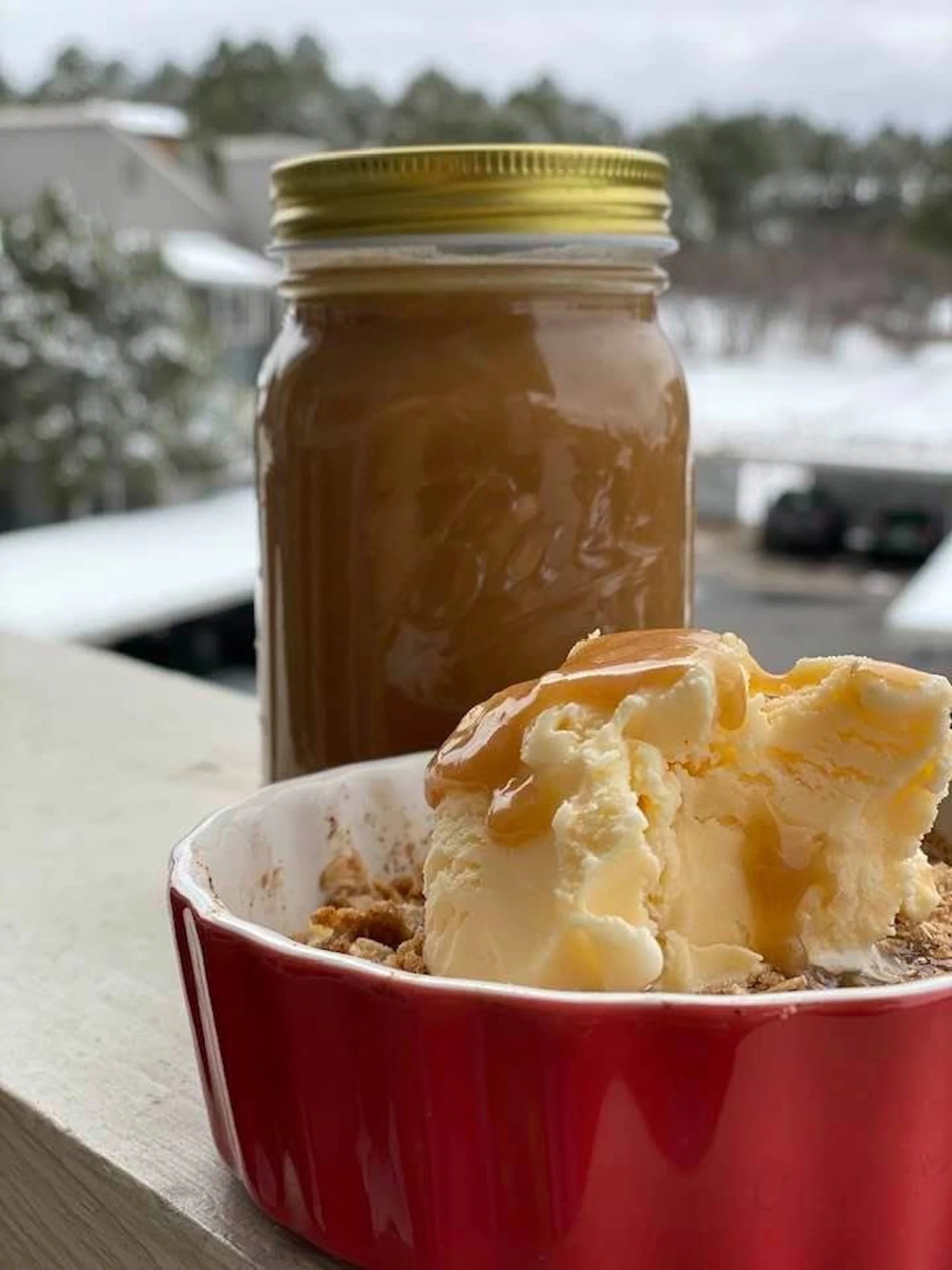 Mason jar full of caramel topping next to orange dish with dessert and ice cream