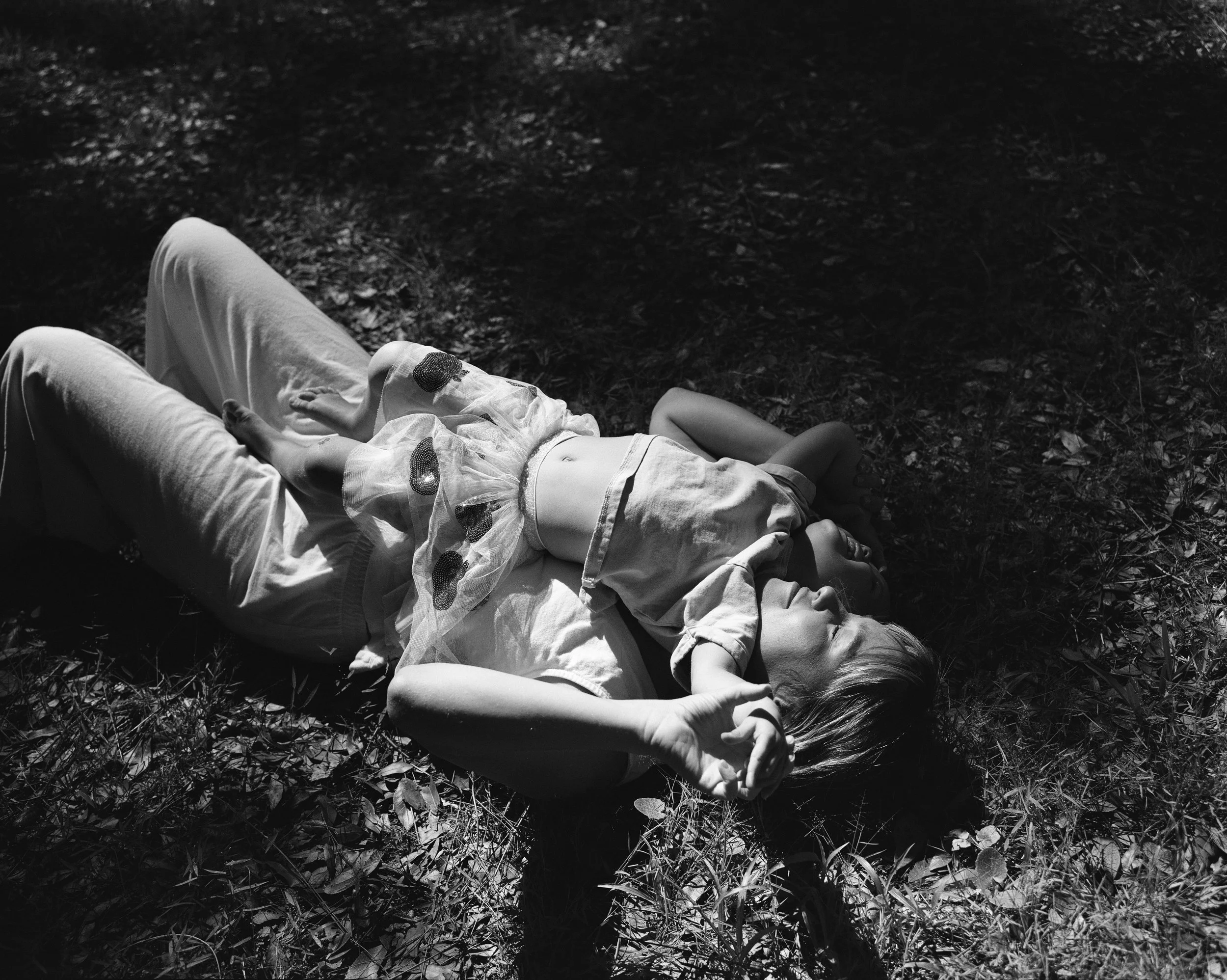 Child lying on the grass in a park at night, wearing light-colored clothing, resting with eyes closed.