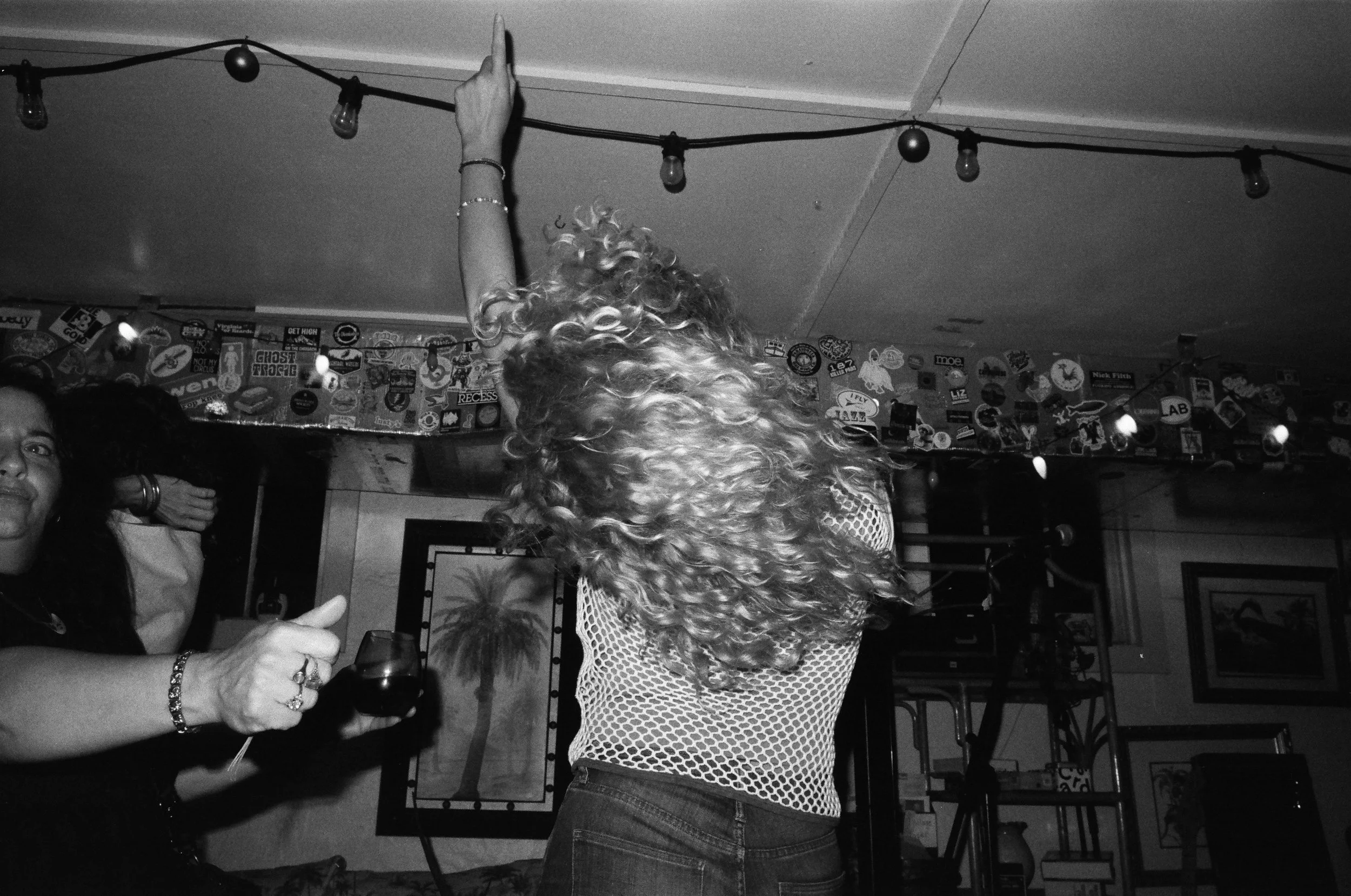 Black and white photo of a woman with curly hair and a fitted top, standing in a room decorated with stickers, raising her arm.