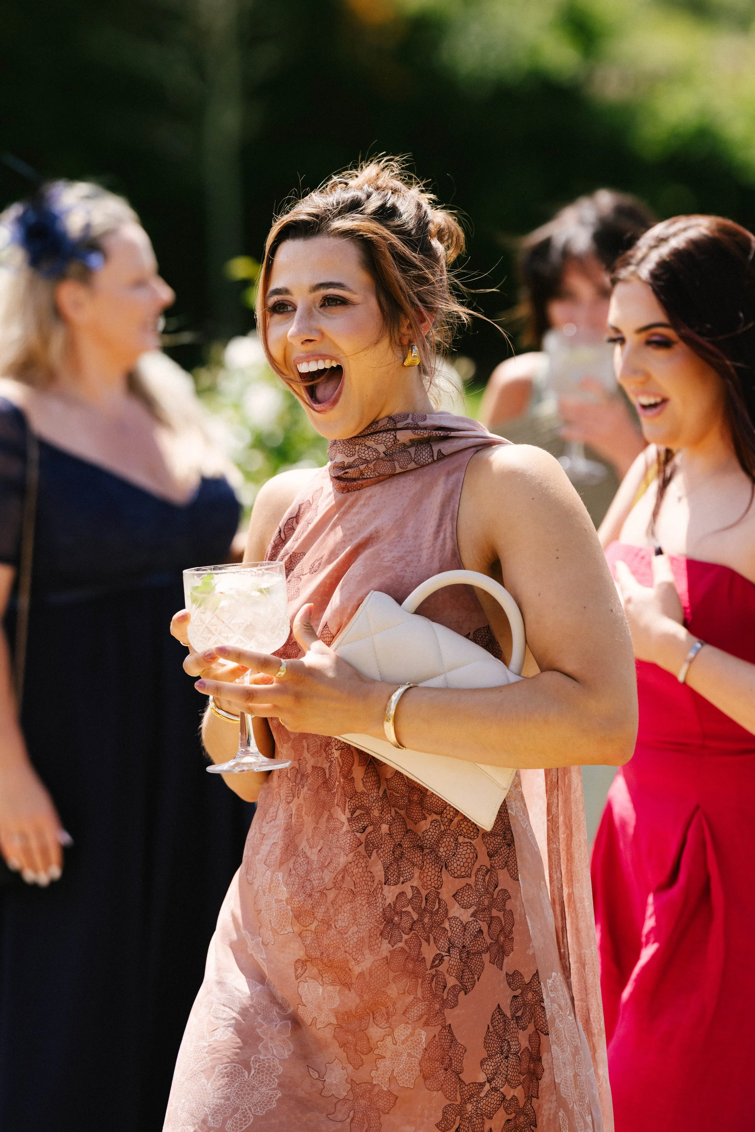 A group of women in colorful dresses at an outdoor social gathering, with one woman in the center smiling and holding a drink.