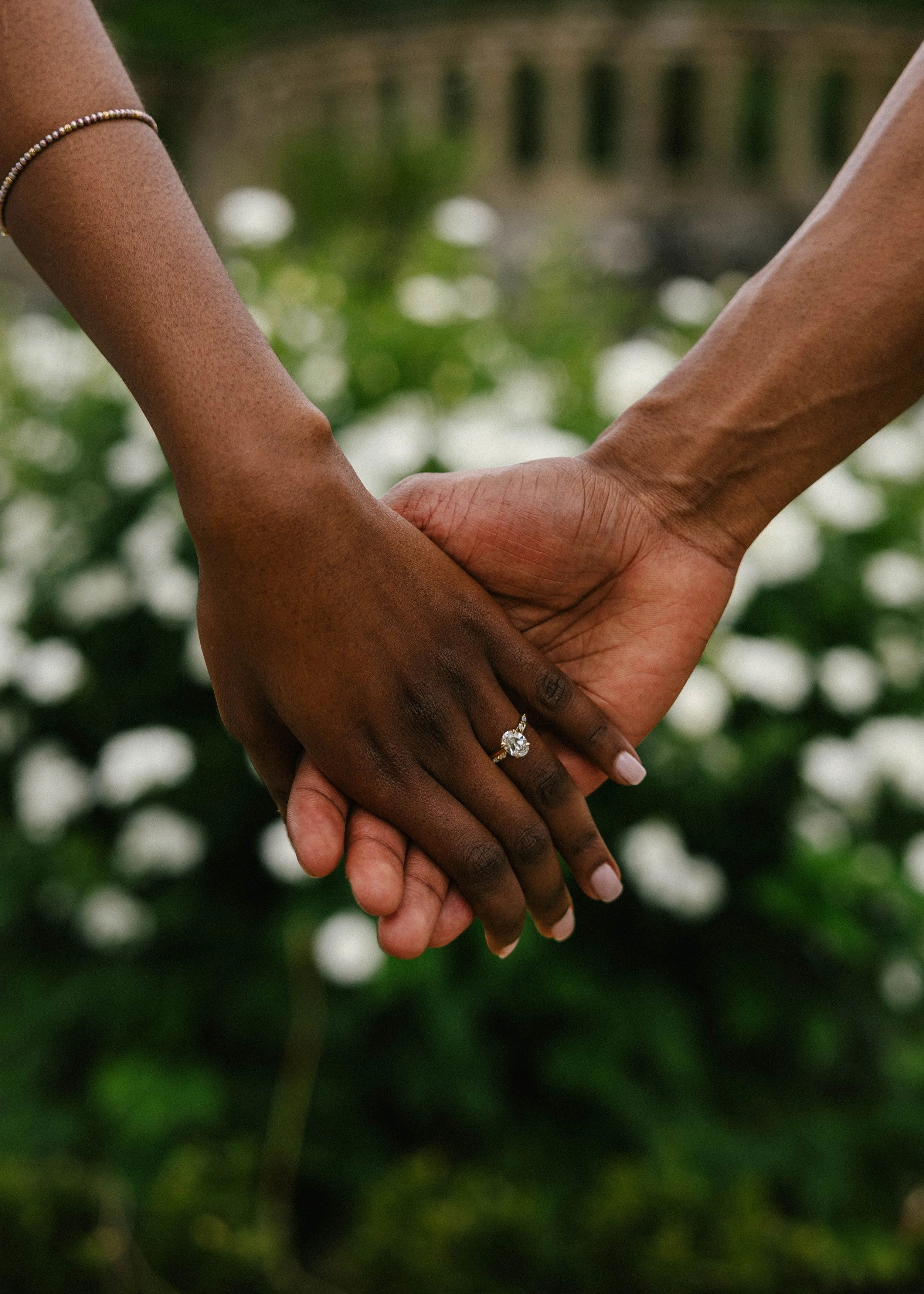 Two people holding hands with one person wearing a ring, with a blurred green background.