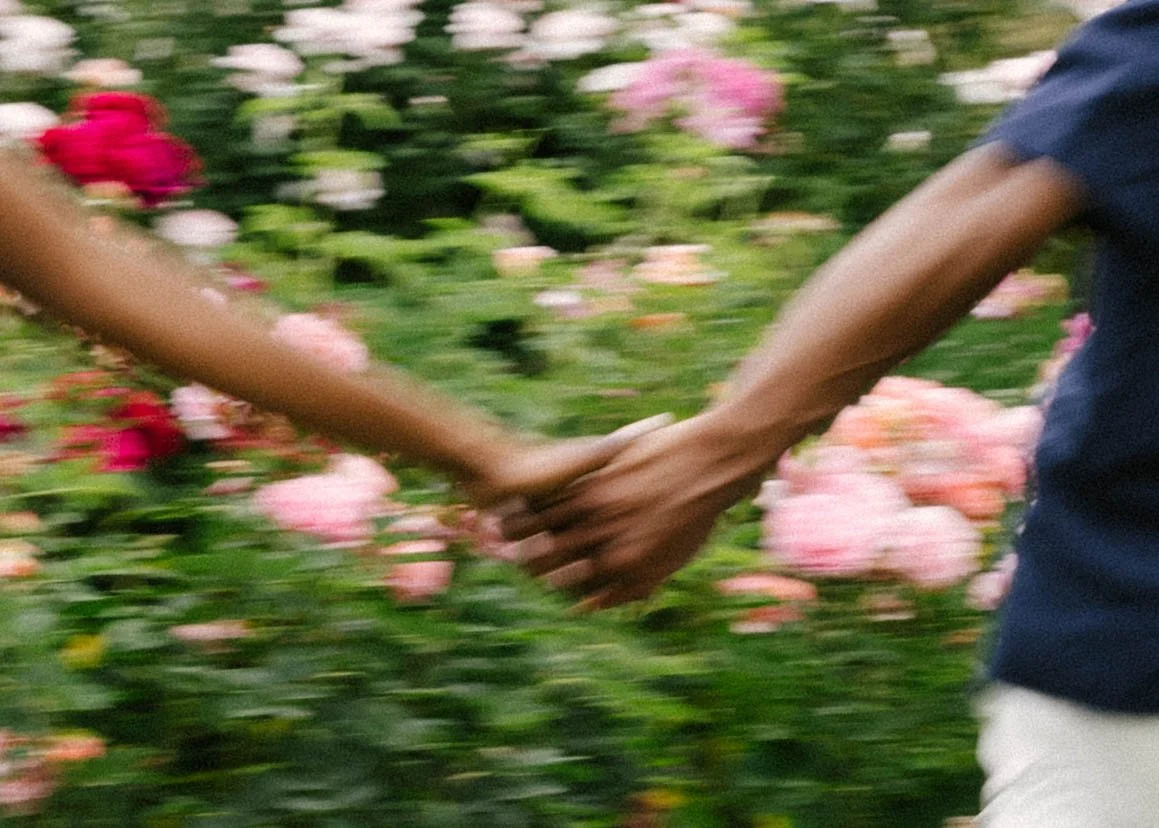 Couple holding hands in a garden with blooming pink and red flowers.