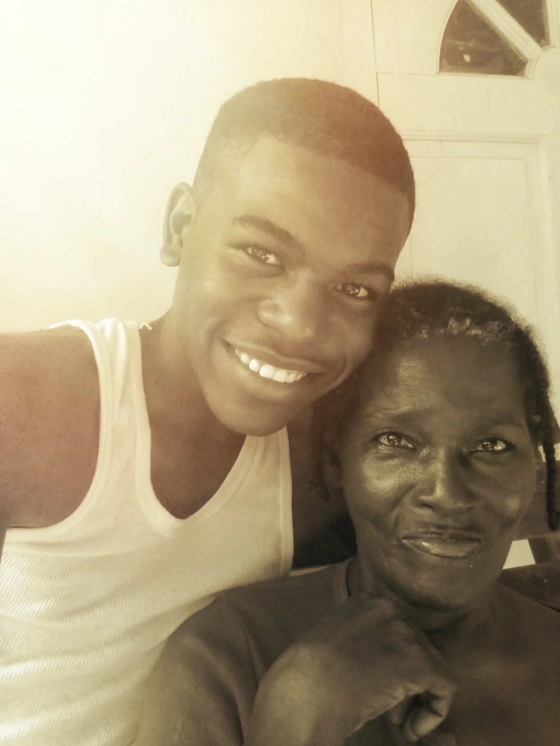 A young man with a short haircut and a woman with braided hair smiling and posing together indoors against a light-colored background.