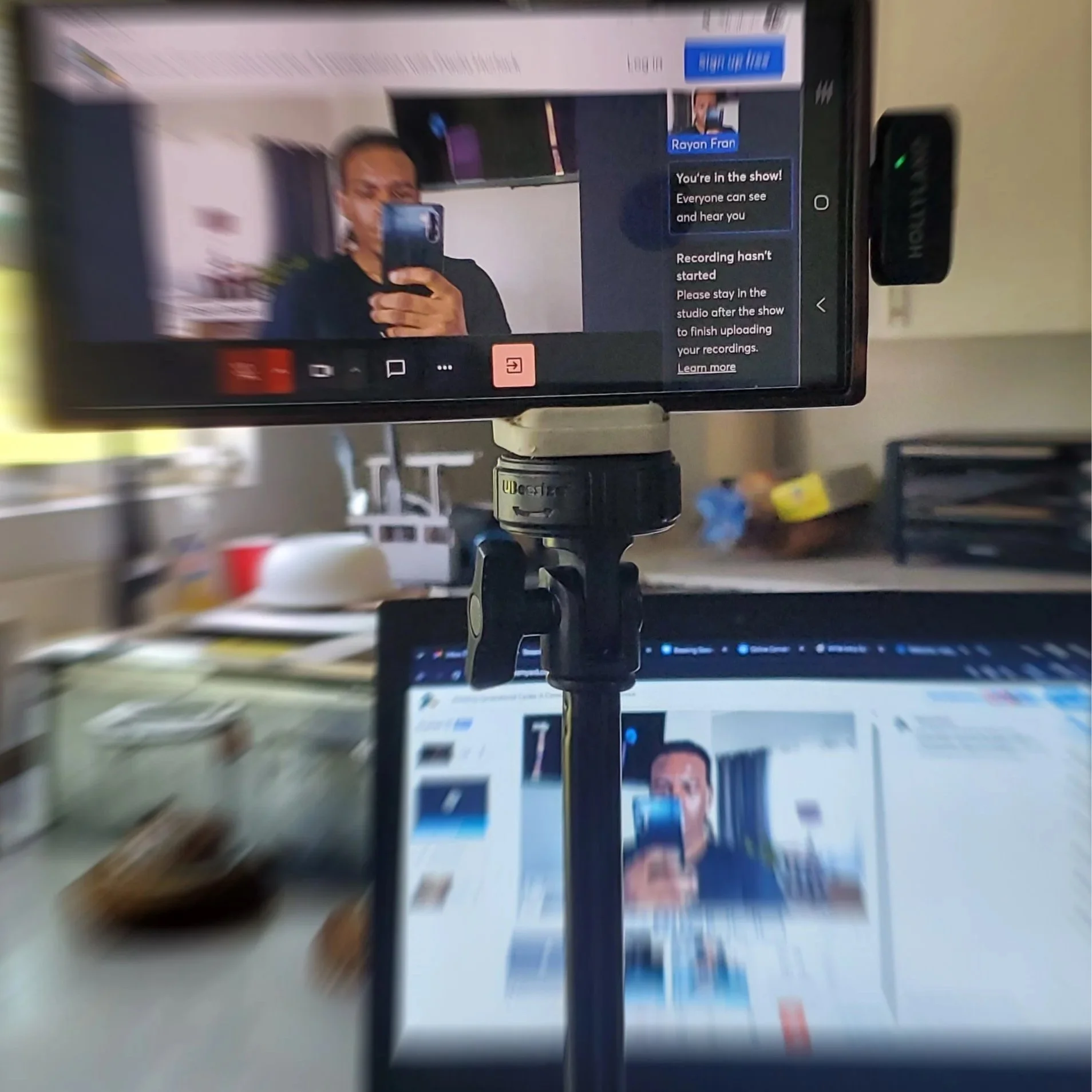 A person taking a selfie in front of a computer screen inside an office or studio environment.