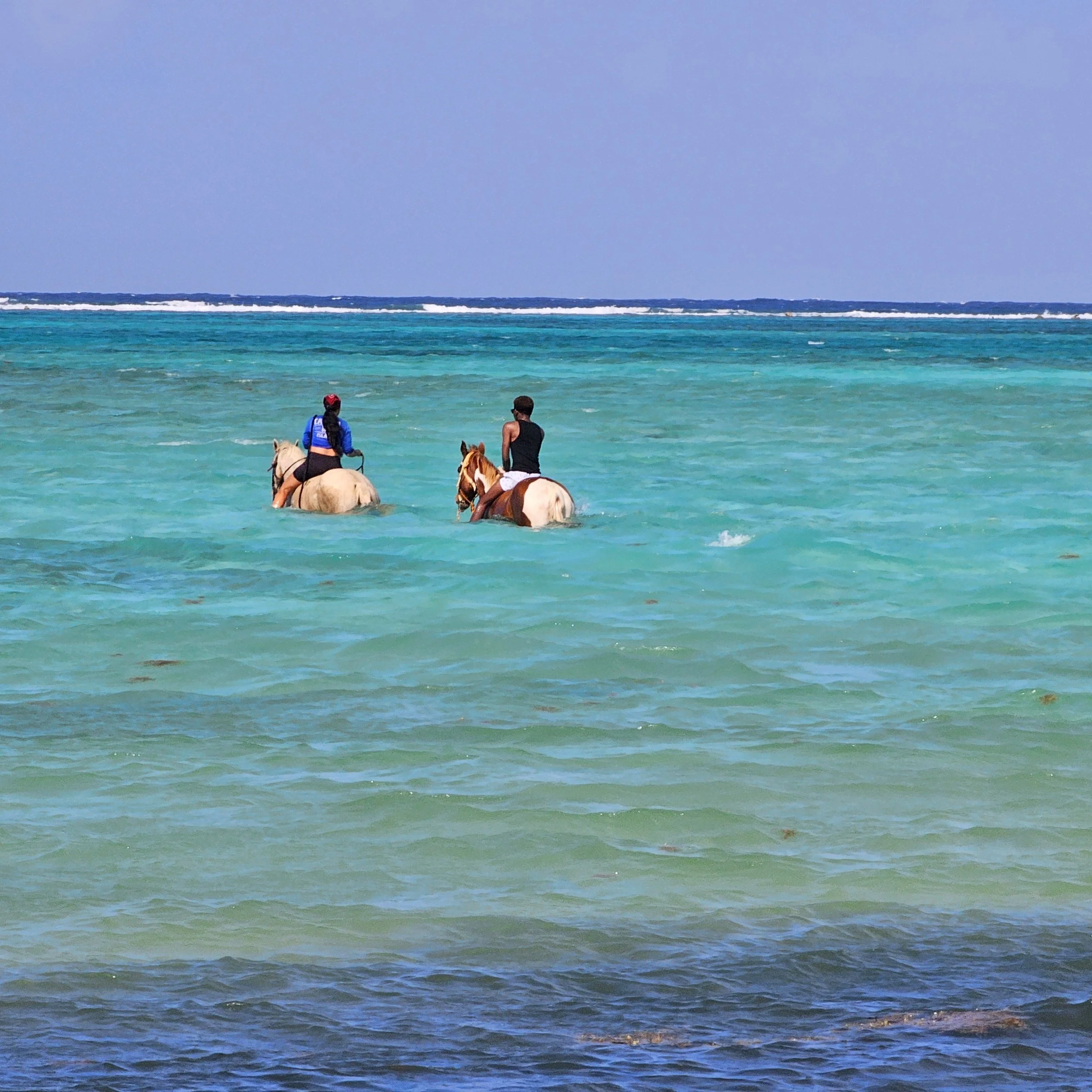 People riding horses in the ocean near the shoreline.