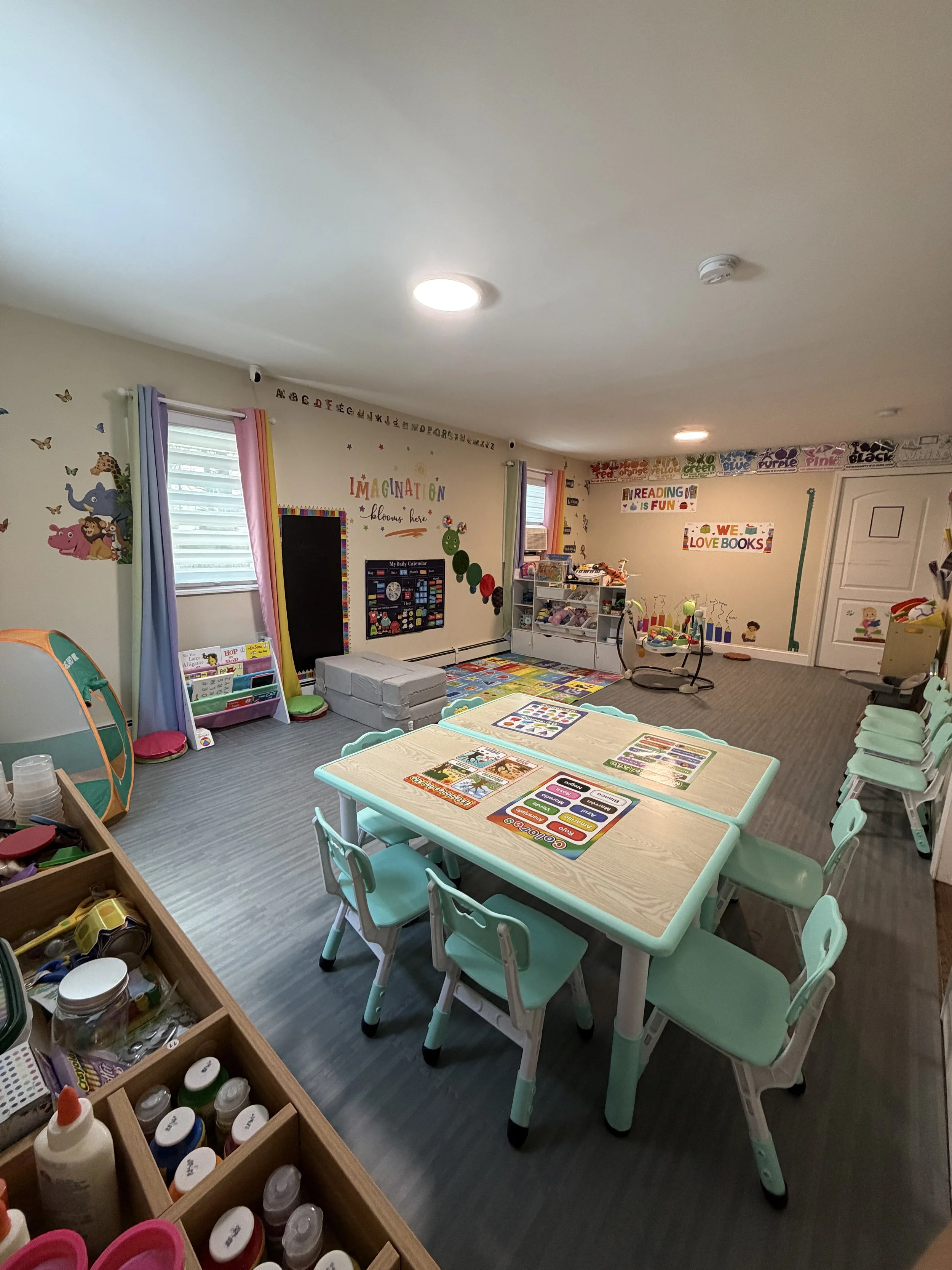 A colorful classroom with small tables and chairs, educational decorations, and shelves filled with toys and books.