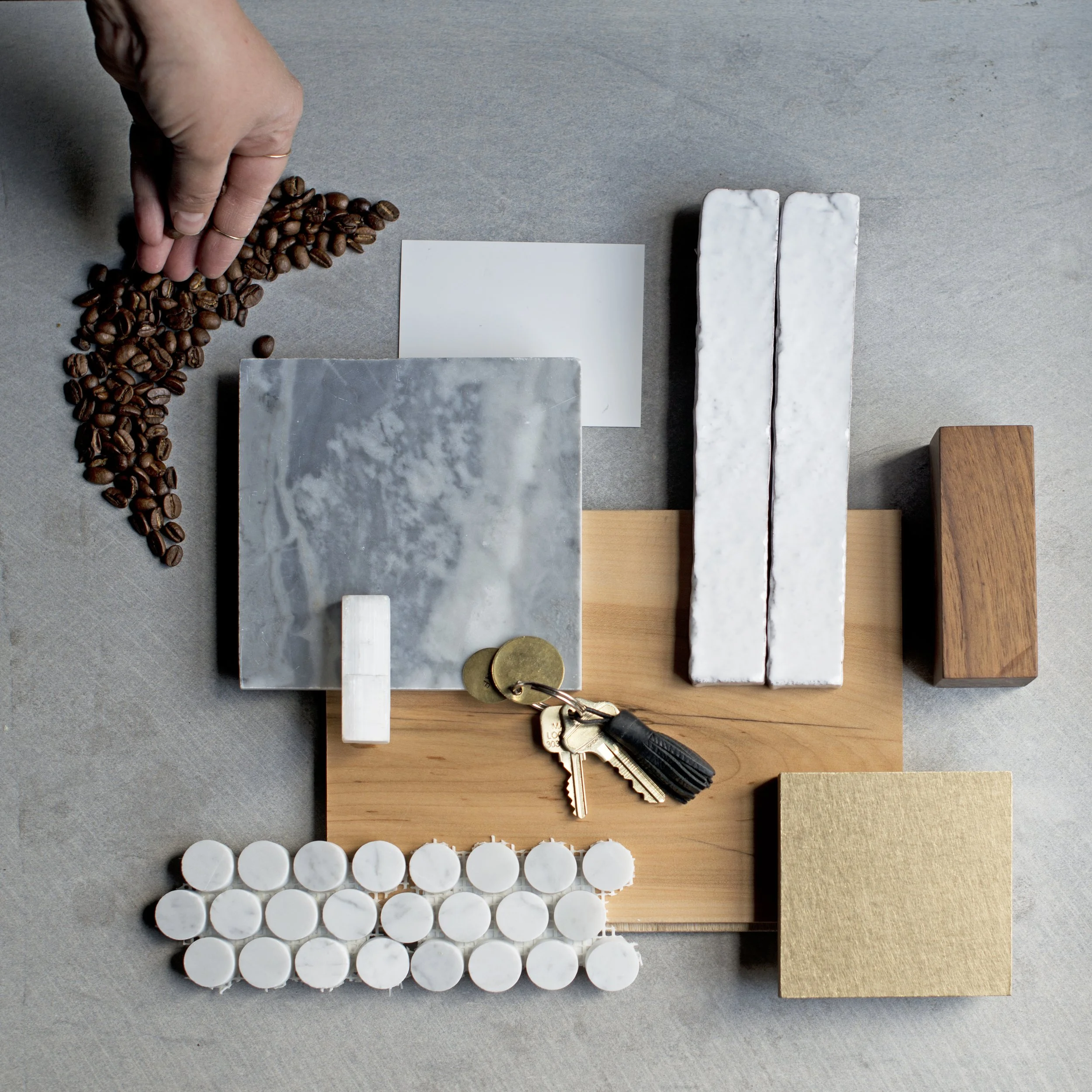 Flat lay of various materials including coffee beans, white candles, marble tiles, wooden and stone samples, and metal keys on a gray surface.