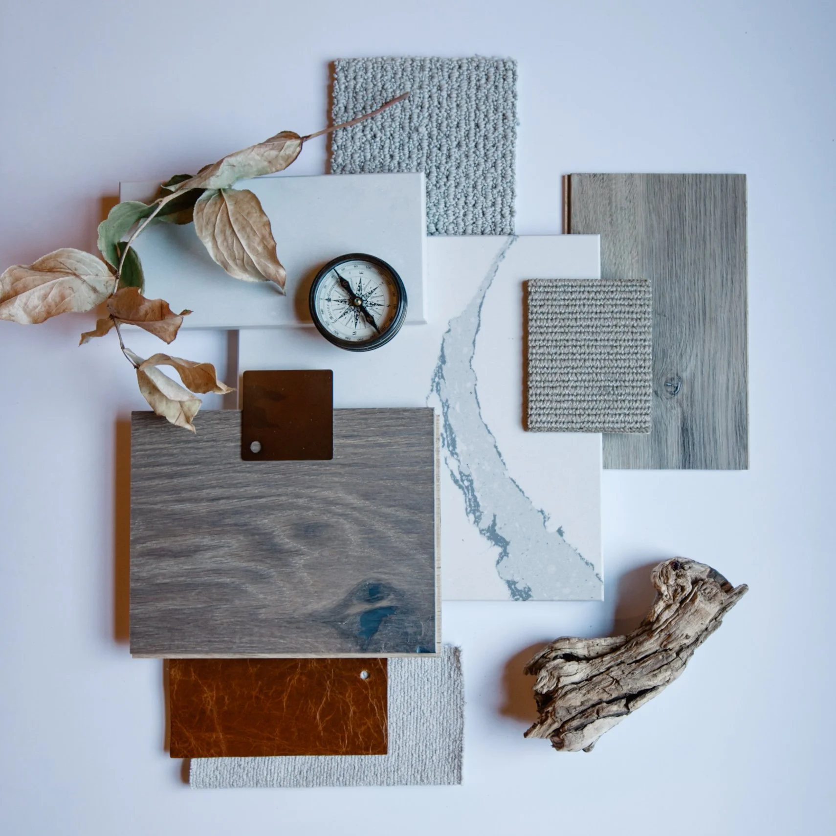 An assortment of material samples including fabric swatches, marble, wood, leather, tile, and a piece of driftwood, arranged on a white background.
