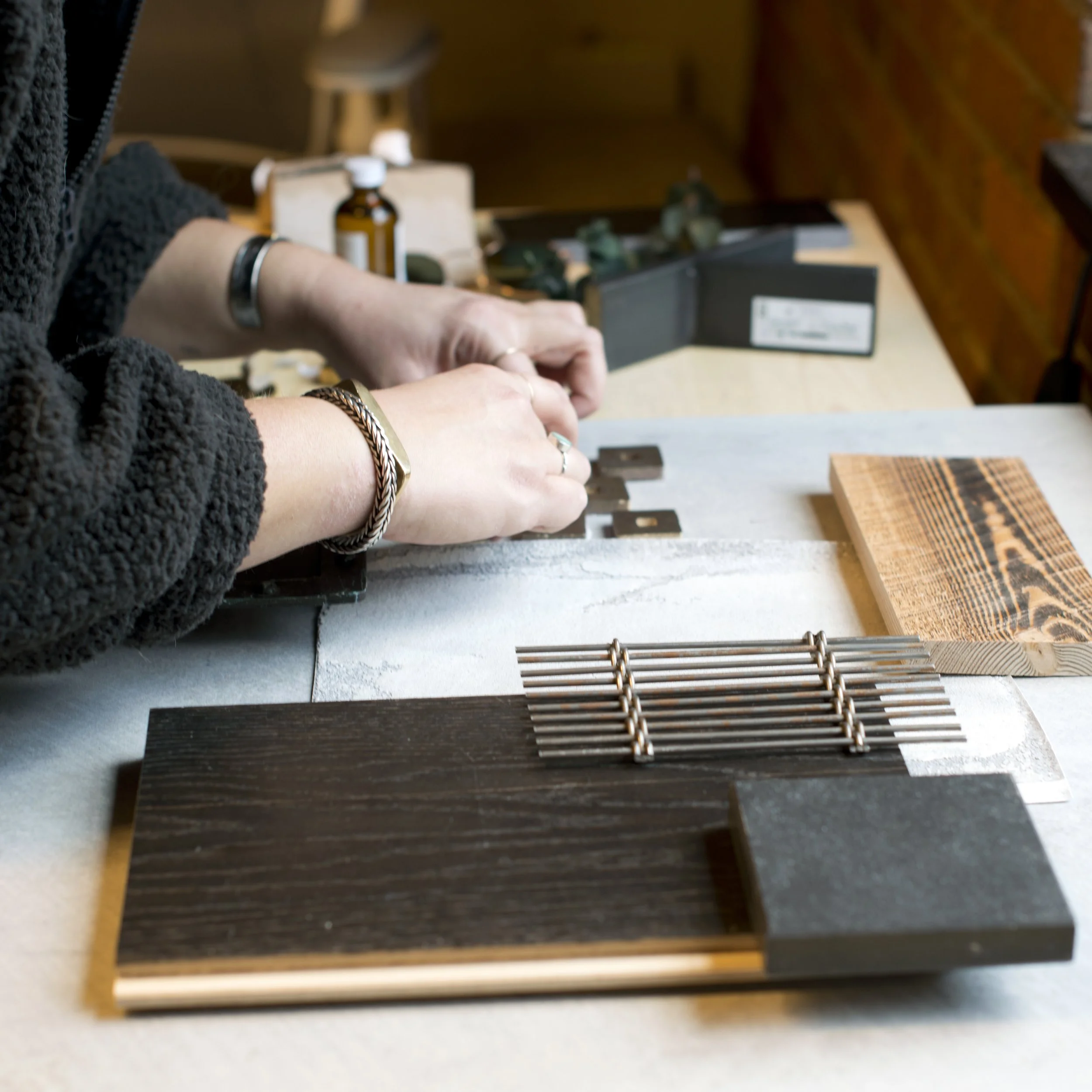 Close-up of a person working on a woodworking project with various tools and samples on a table.