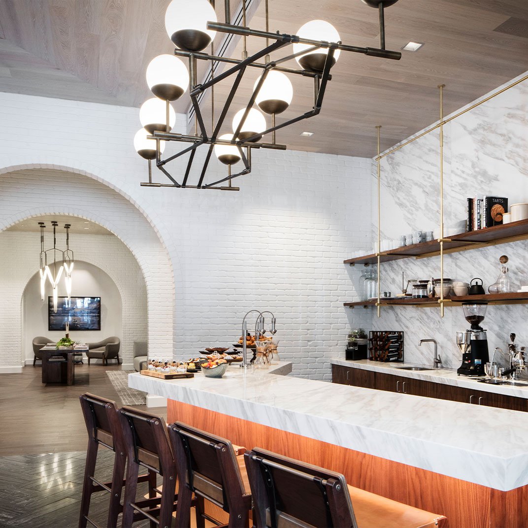 Modern kitchen with a white marble island, dark wood cabinetry, open shelves with dishes and books, and a contemporary black chandelier with globe lights.
