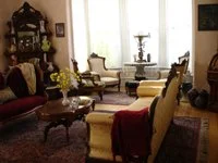 Living room with antique furniture, including armchairs, a coffee table, and a side table, with a large window letting in natural light.