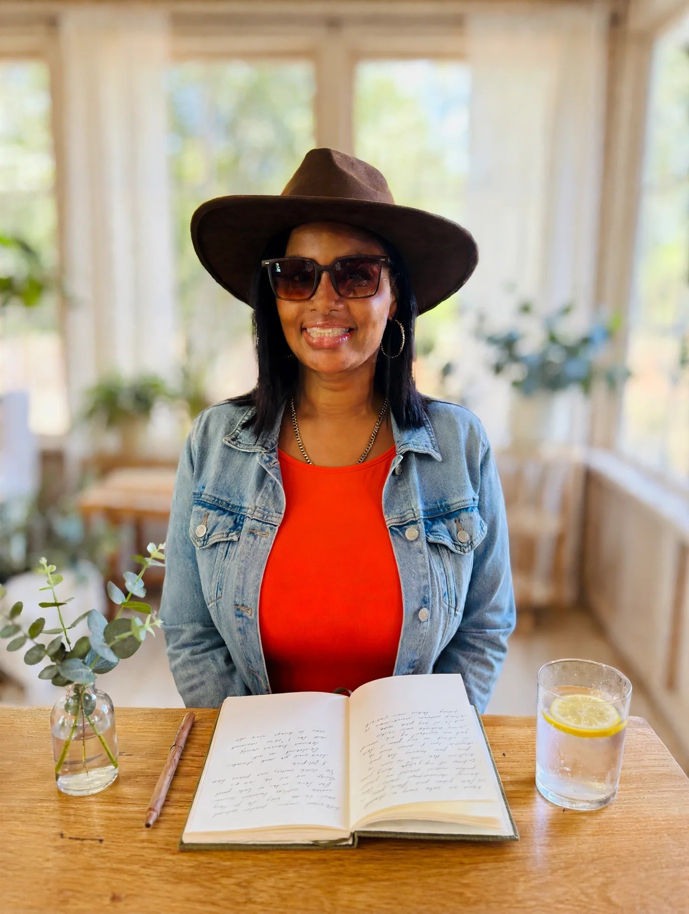 Smiling San Antonio doula sitting at a table with a cup of tea, a glass of water, and a journal during a client consultation.