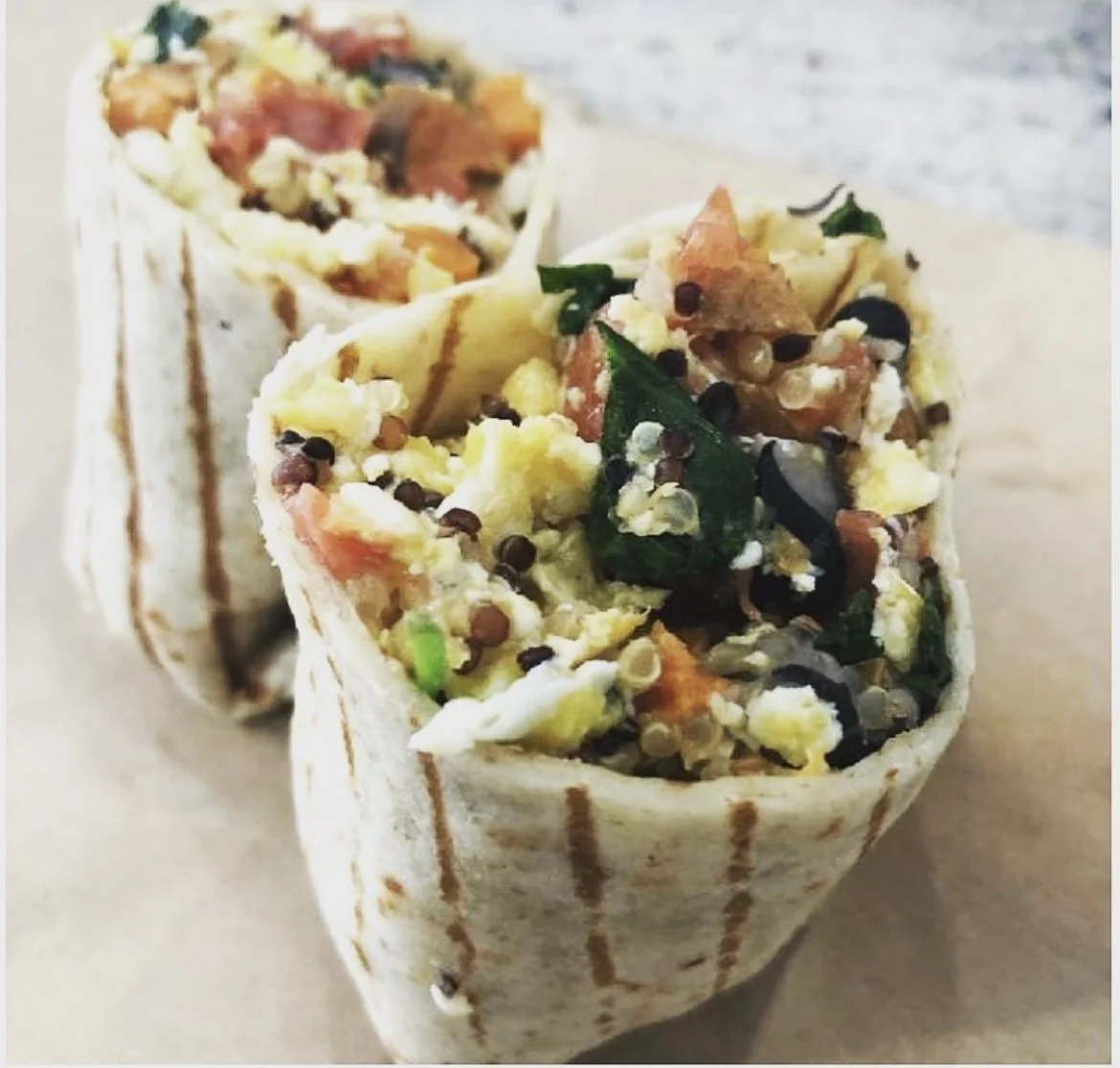 Two grilled wraps filled with scrambled eggs, spinach, black beans, cheese, and diced vegetables.