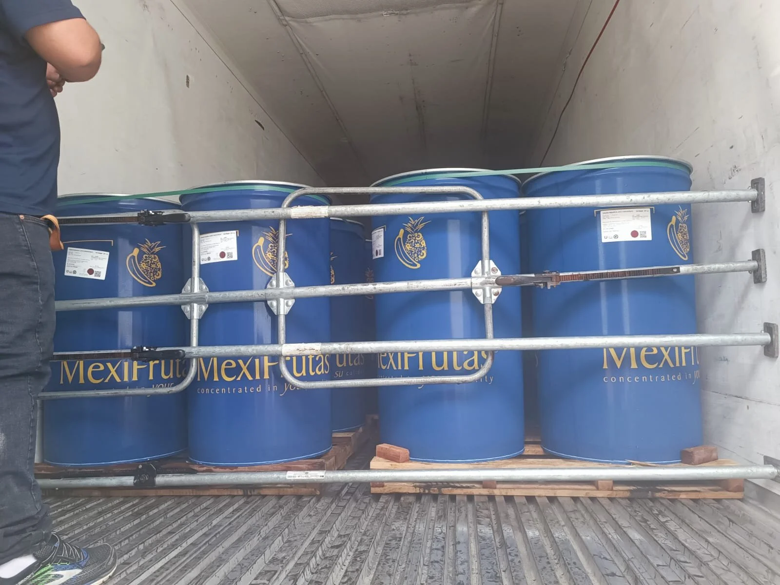 Barriles azules con el logotipo de Mexifrut, apilados en un camión, asegurados con una estructura metálica para transporte.