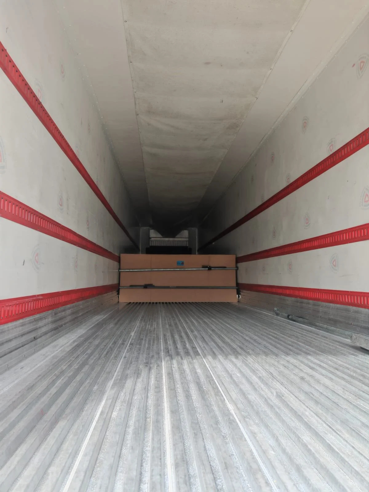 Vista interior de la caja de una camioneta de carga vacía con paredes forradas y piso metálico, con una pared de caja de carga y una carga literal en la parte trasera.