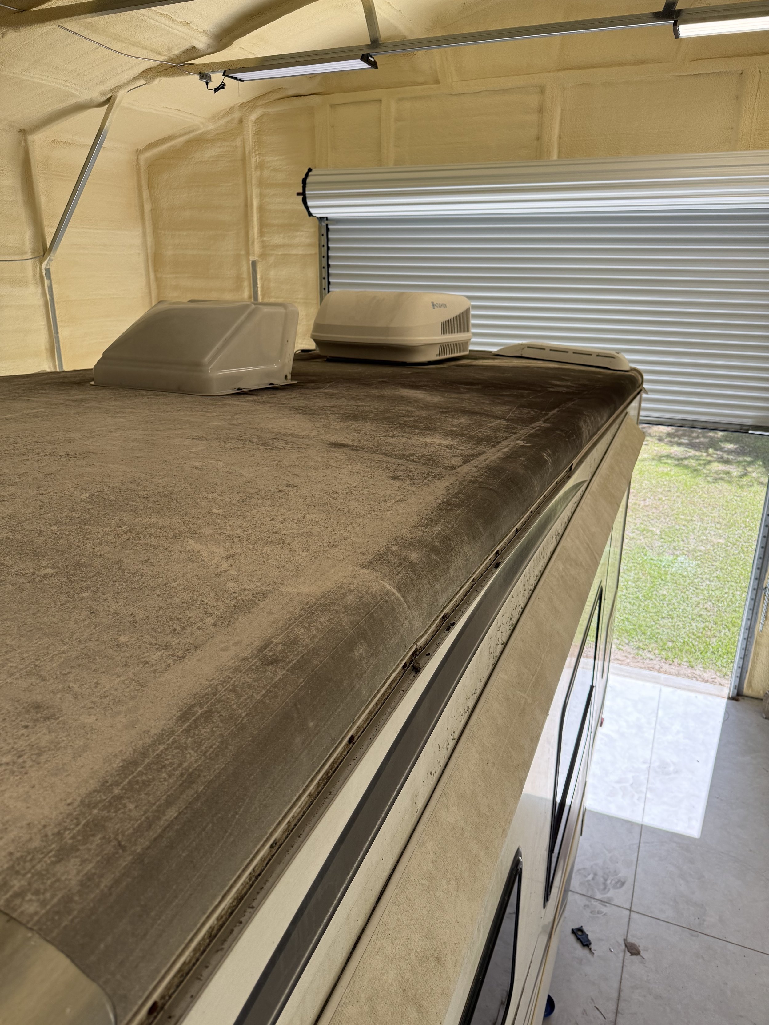 Side view of an RV with a dusty, weathered roof, and a partially visible outdoor area with a tiled patio and green grass.