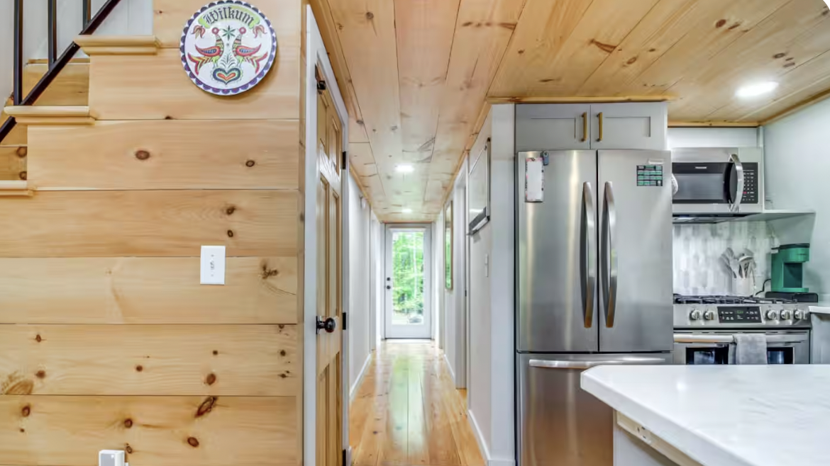 View of a kitchen with wooden walls, stainless steel appliances, and a hallway leading outside through a glass door.